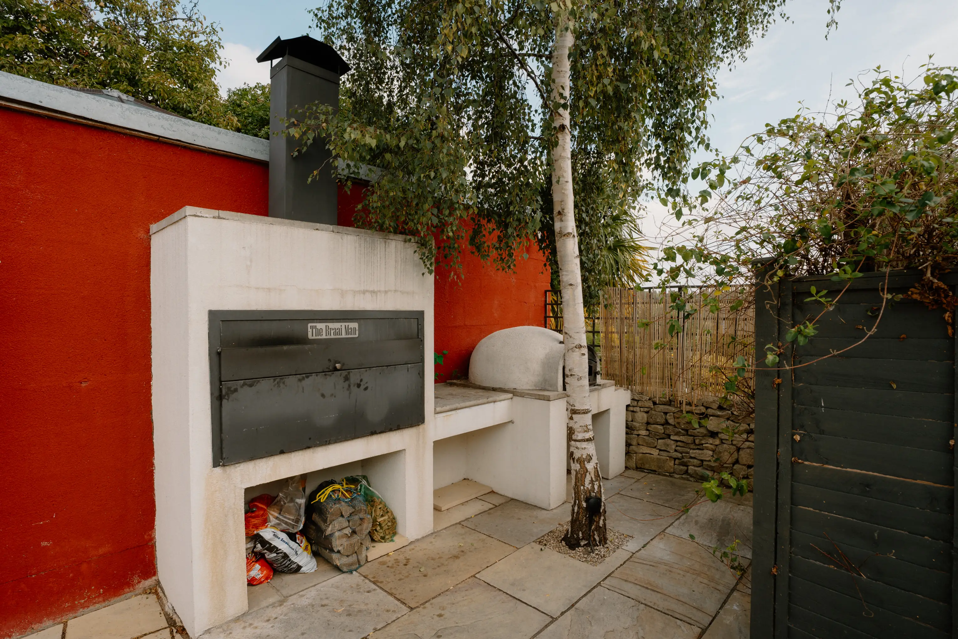 Alfresco kitchen at ARC Painswick with a pizza oven and Braii against a red wall on the stone patio