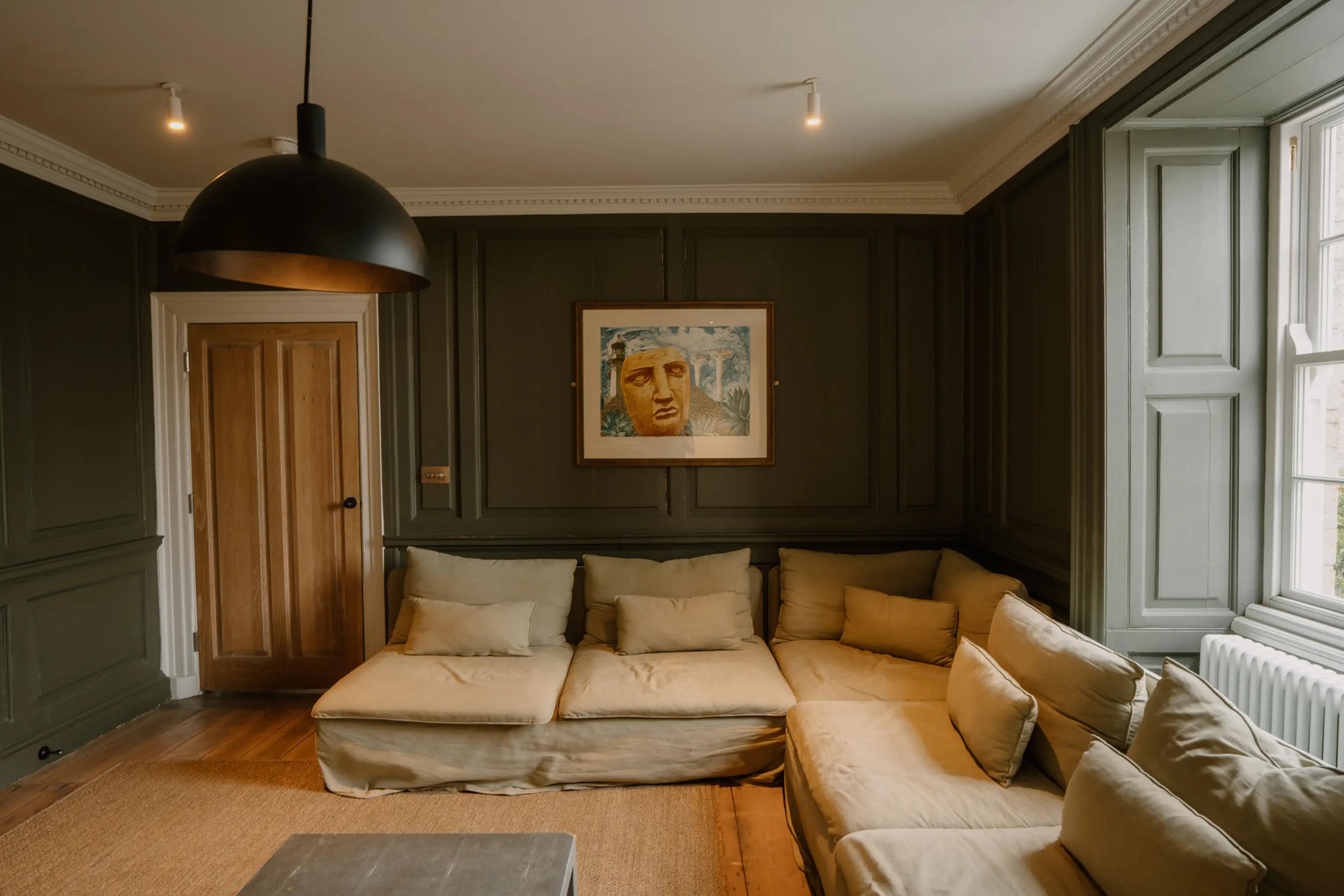 Sage-green lounge at ARC Padstow with a large corner sofa and pendant light