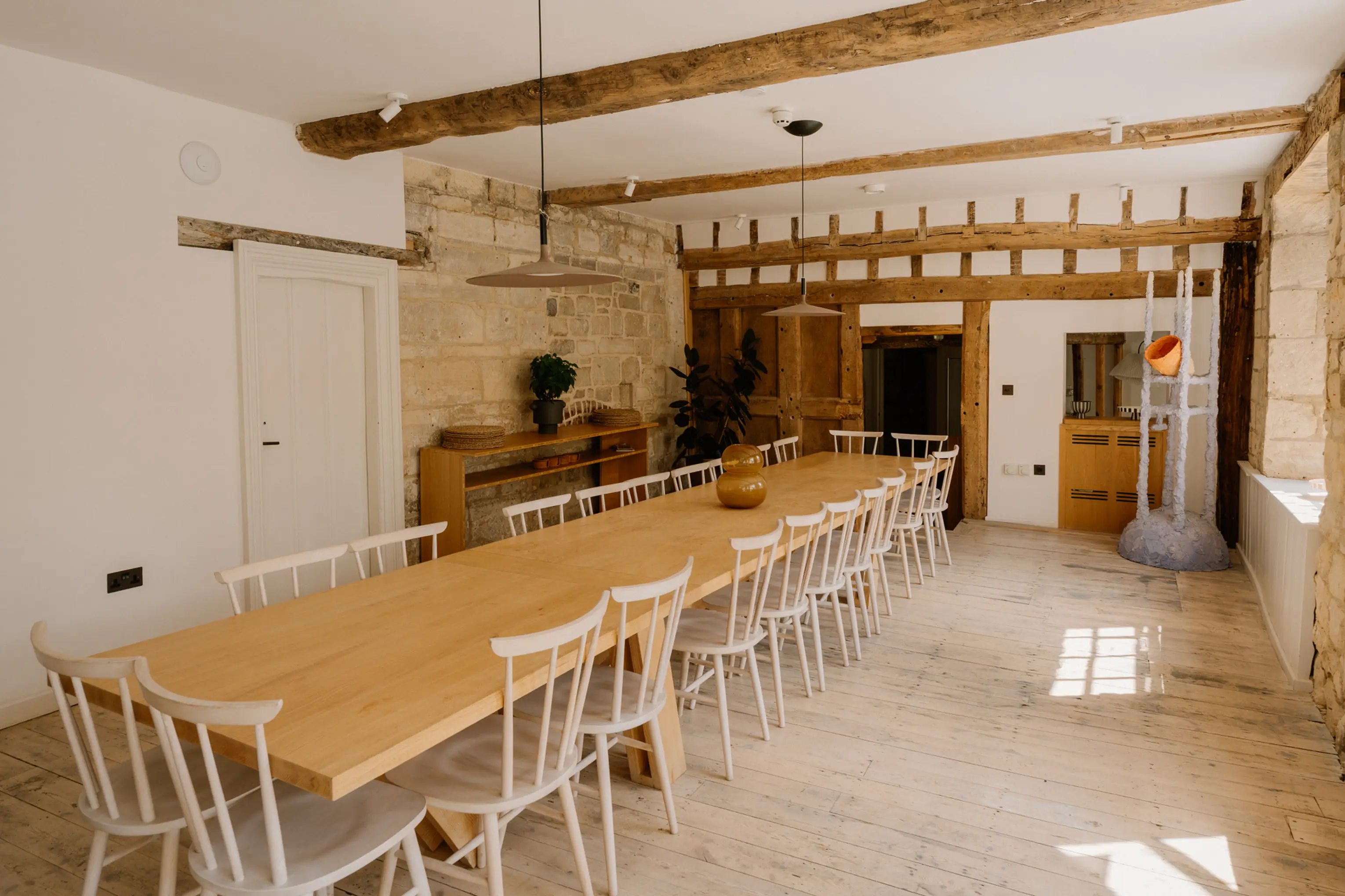 Bright dining room at ARC Painswick with a long table, white chairs and exposed beams