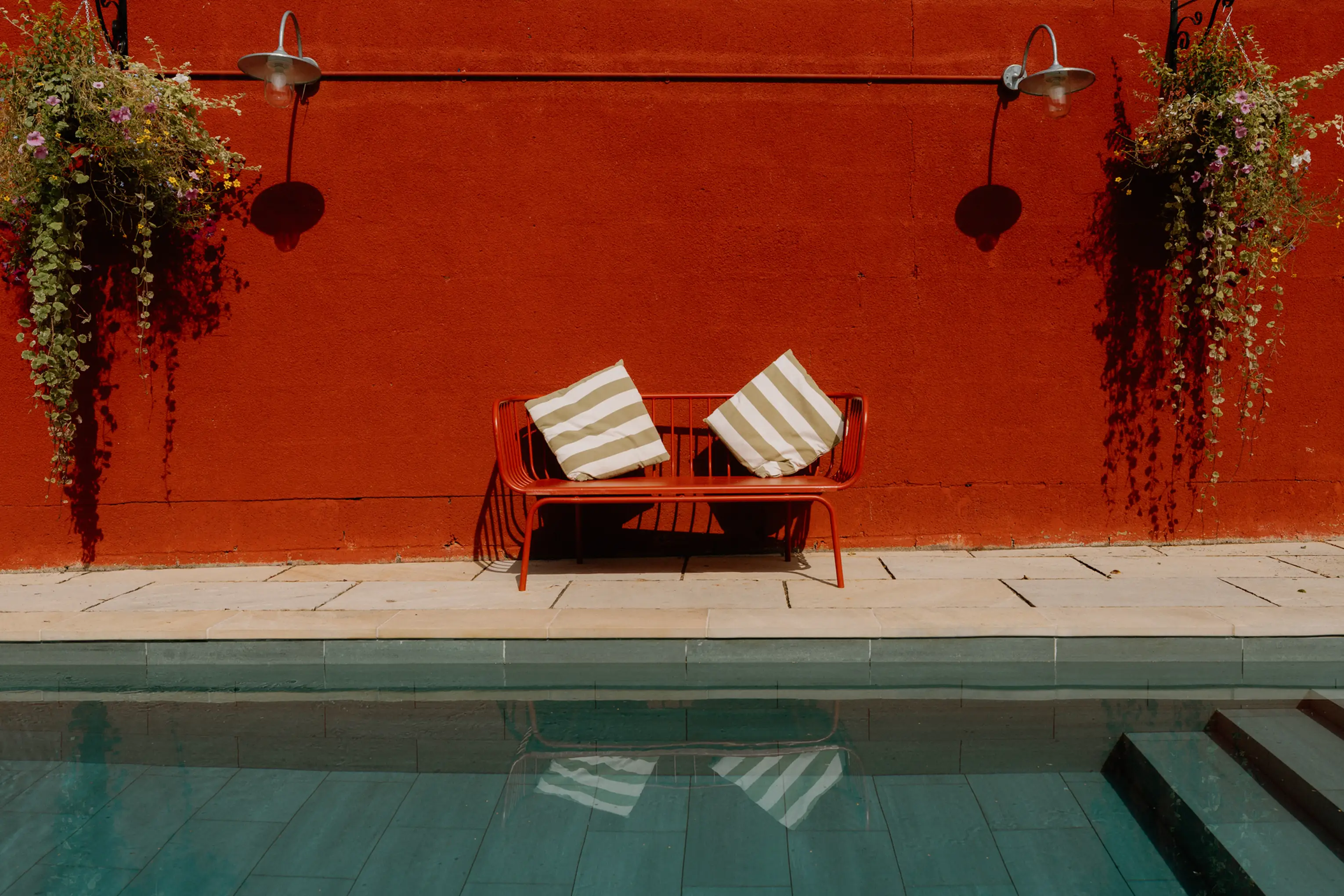 Sun loungers beside the outdoor pool against a red wall at ARC Painswick