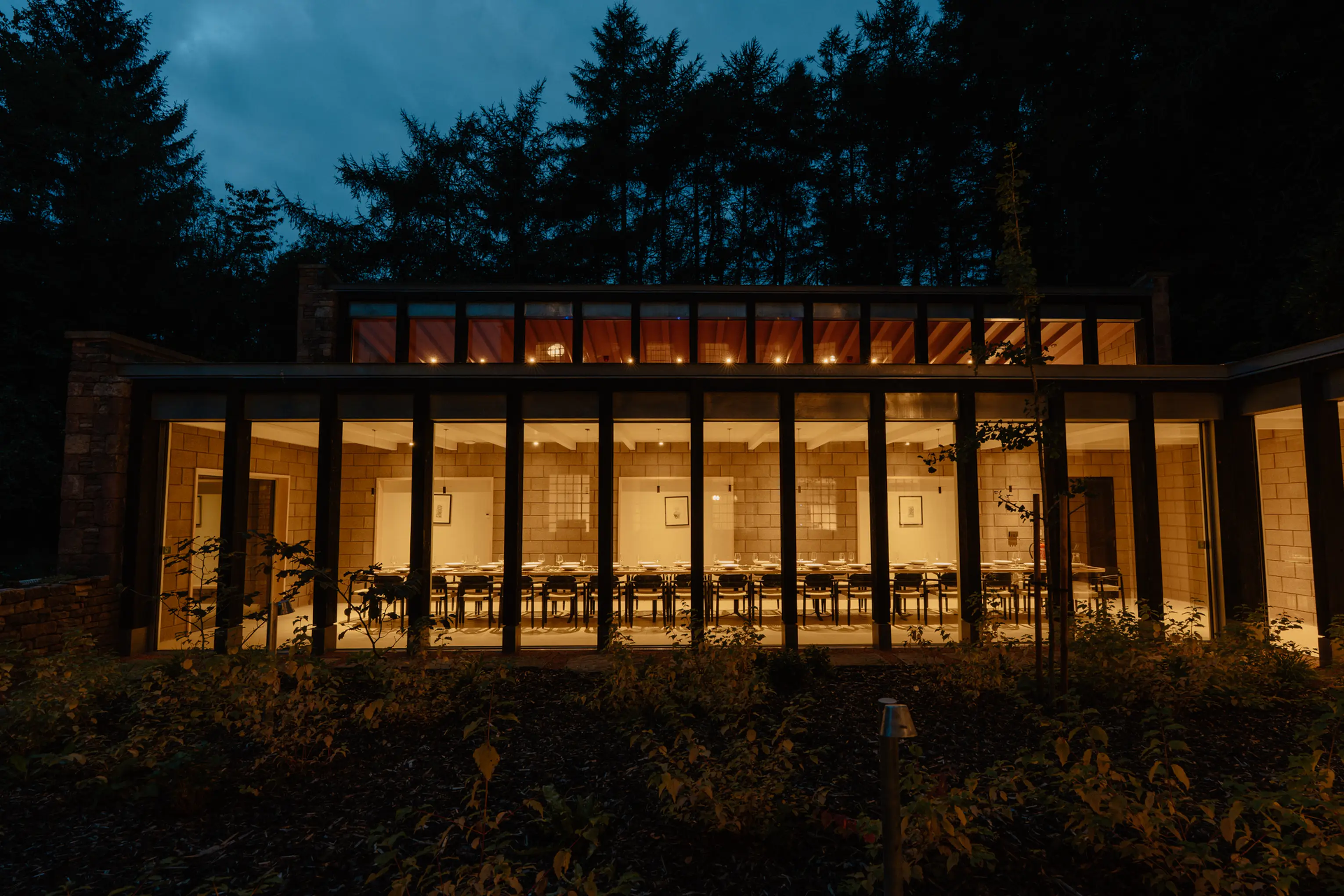 ARC Peaks lit at dusk, the glazed extension glowing against the Peak District woodland