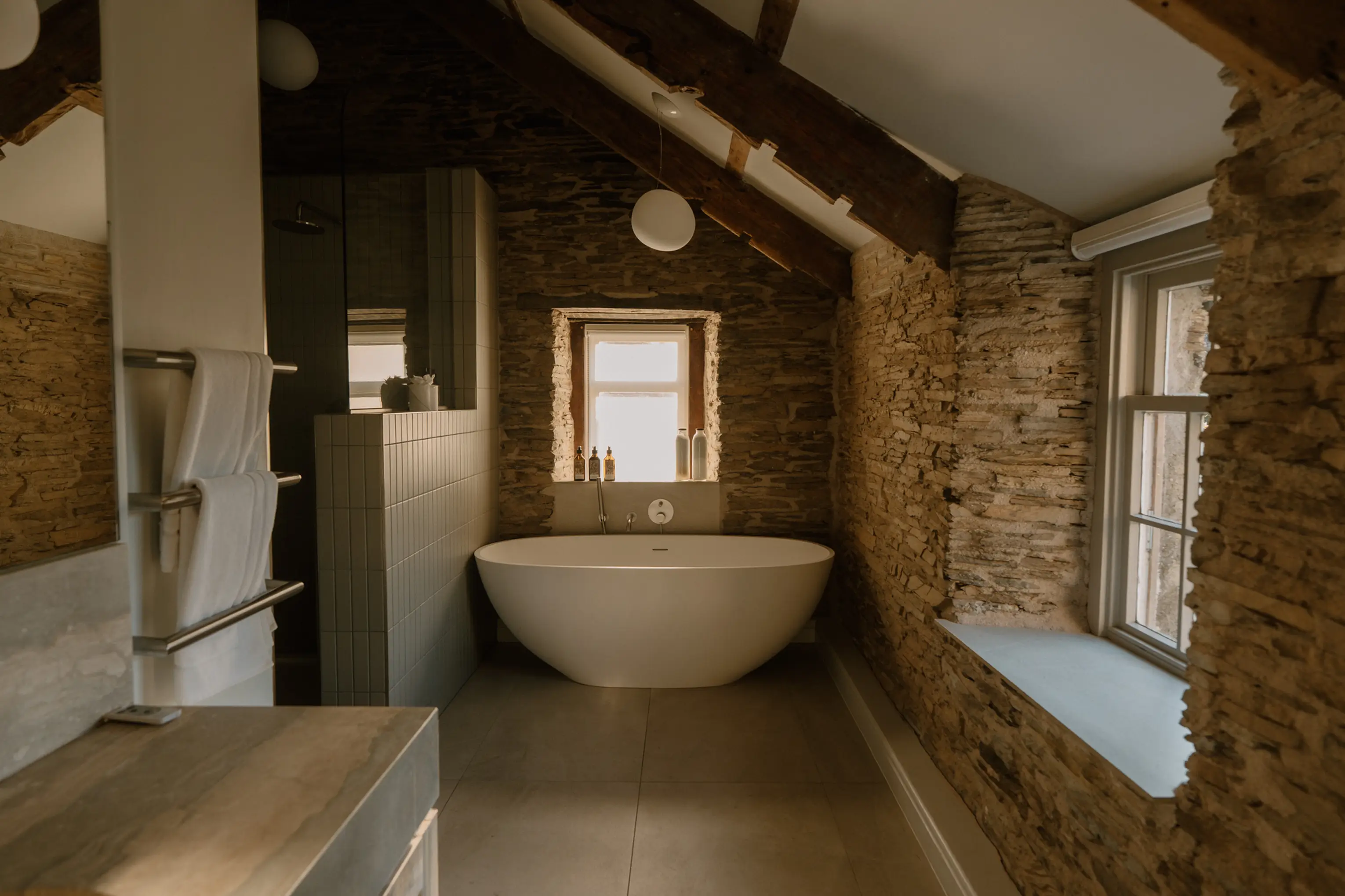Bathroom at ARC Padstow with a freestanding tub against an exposed stone wall and window