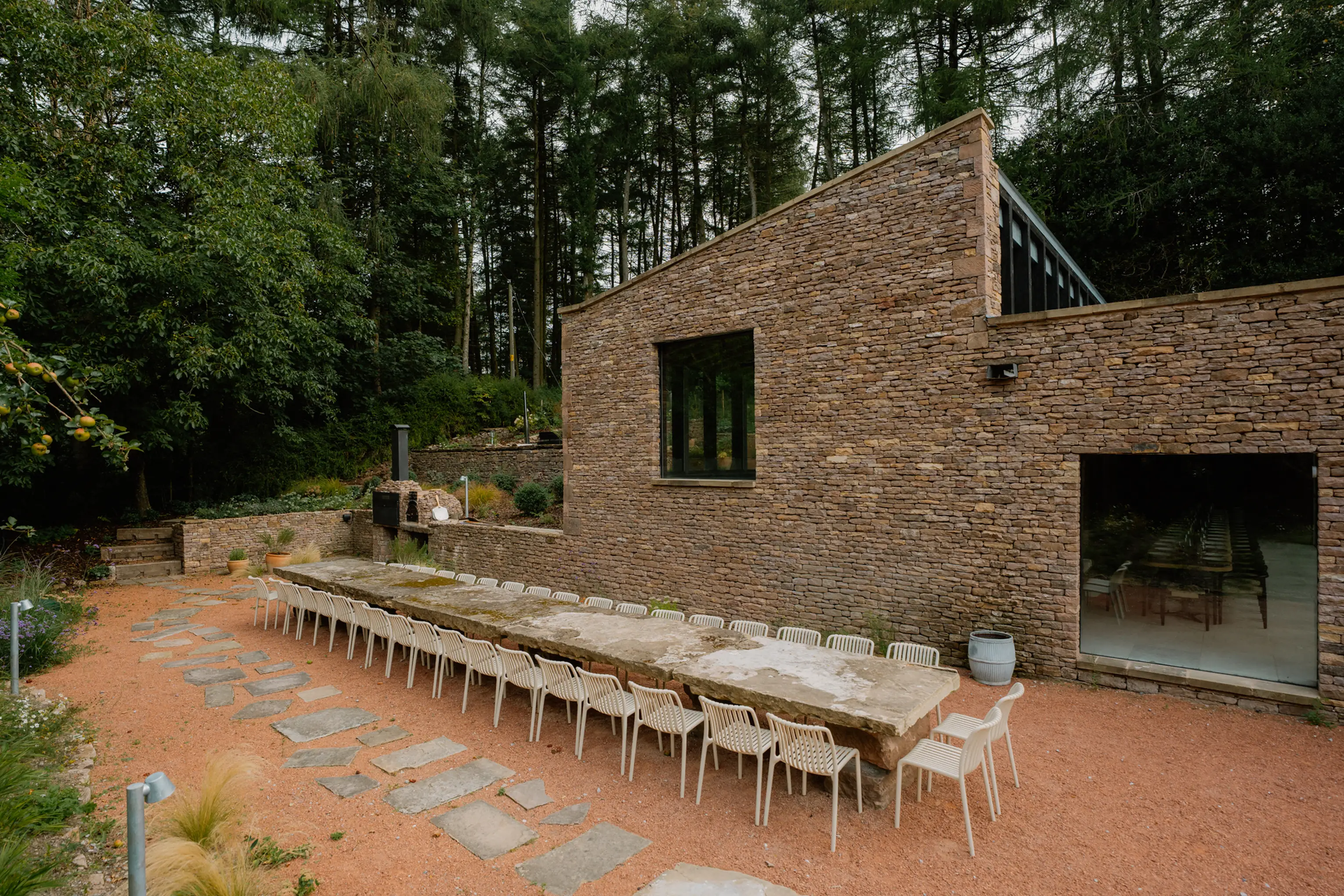 Long stone outdoor dining table on the terrace at ARC Peaks, backed by woodland