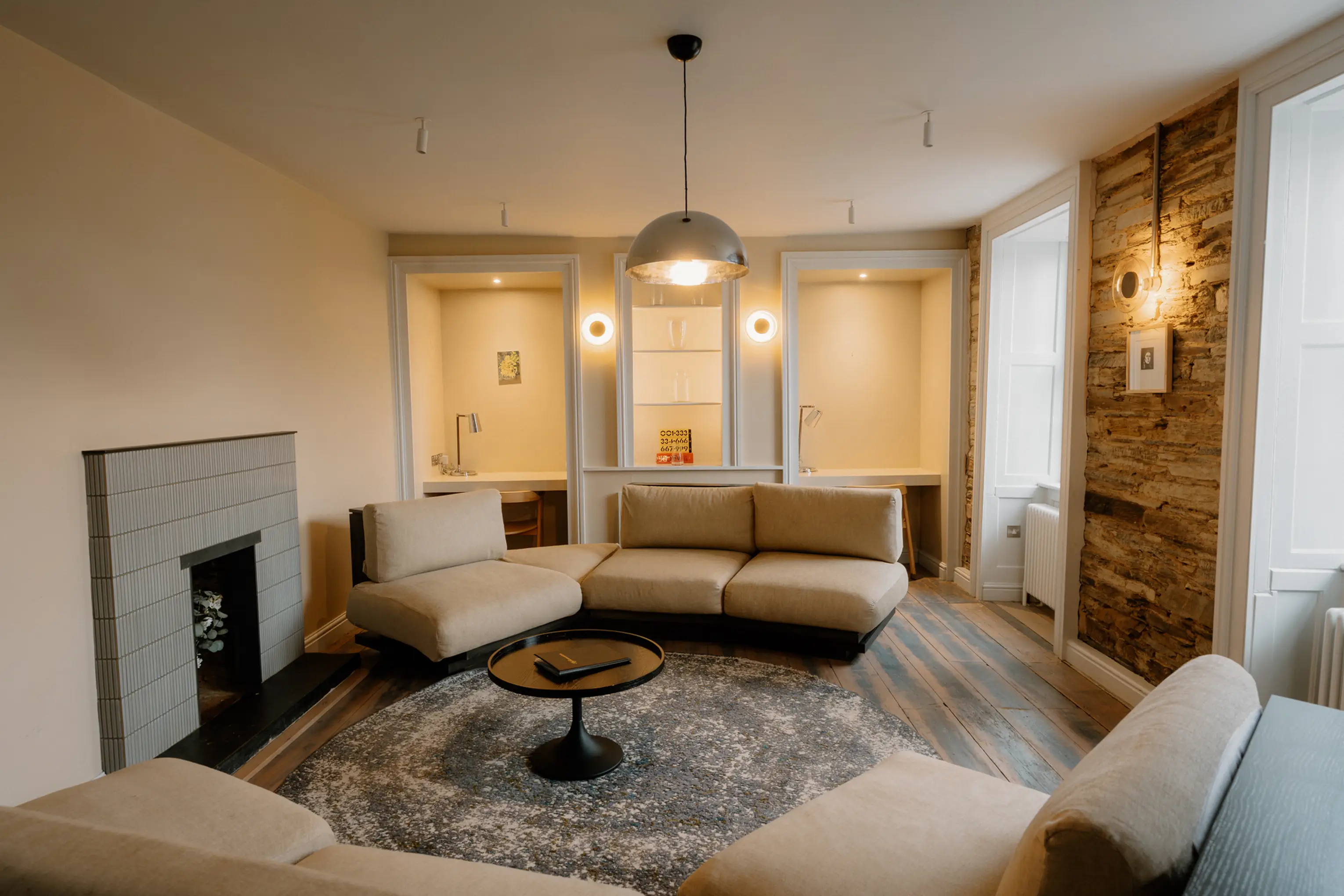Sitting room at ARC Padstow with sofas, a low coffee table and a fireplace beneath large windows