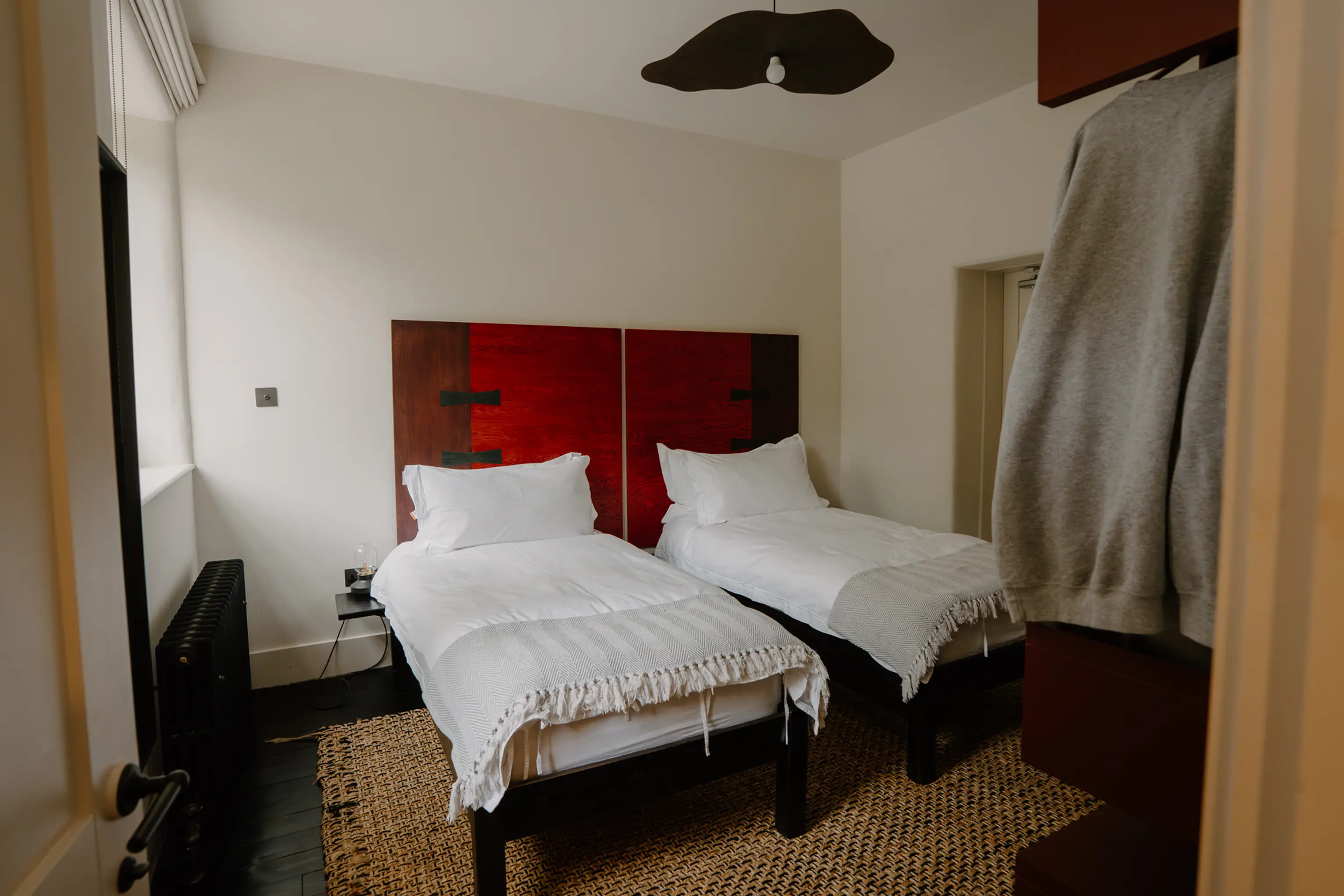 Twin bedroom at ARC Peaks with two single beds, red headboards and a hanging rail