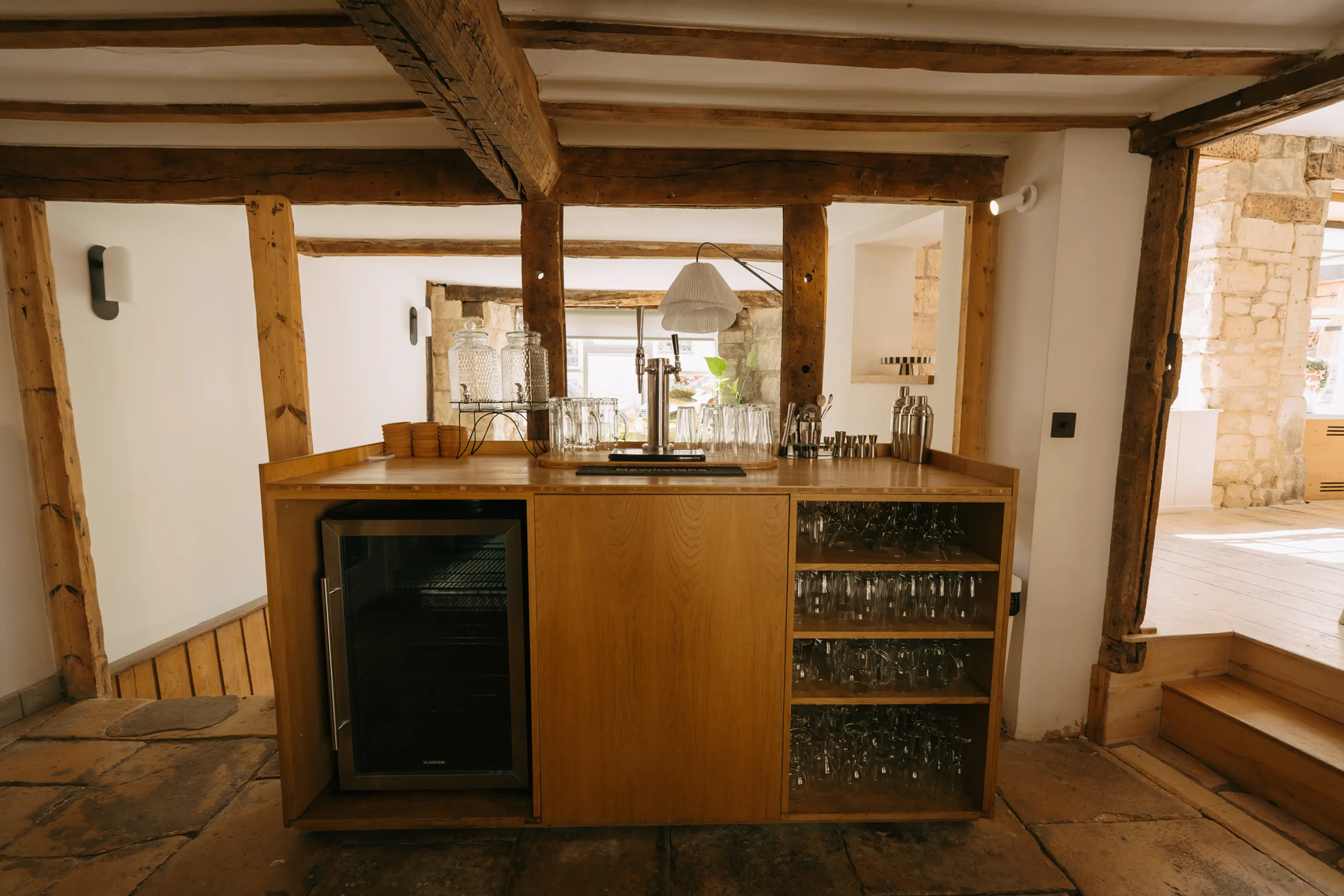 Kitchen and bar at ARC Painswick with a wine fridge, open shelving and exposed beams