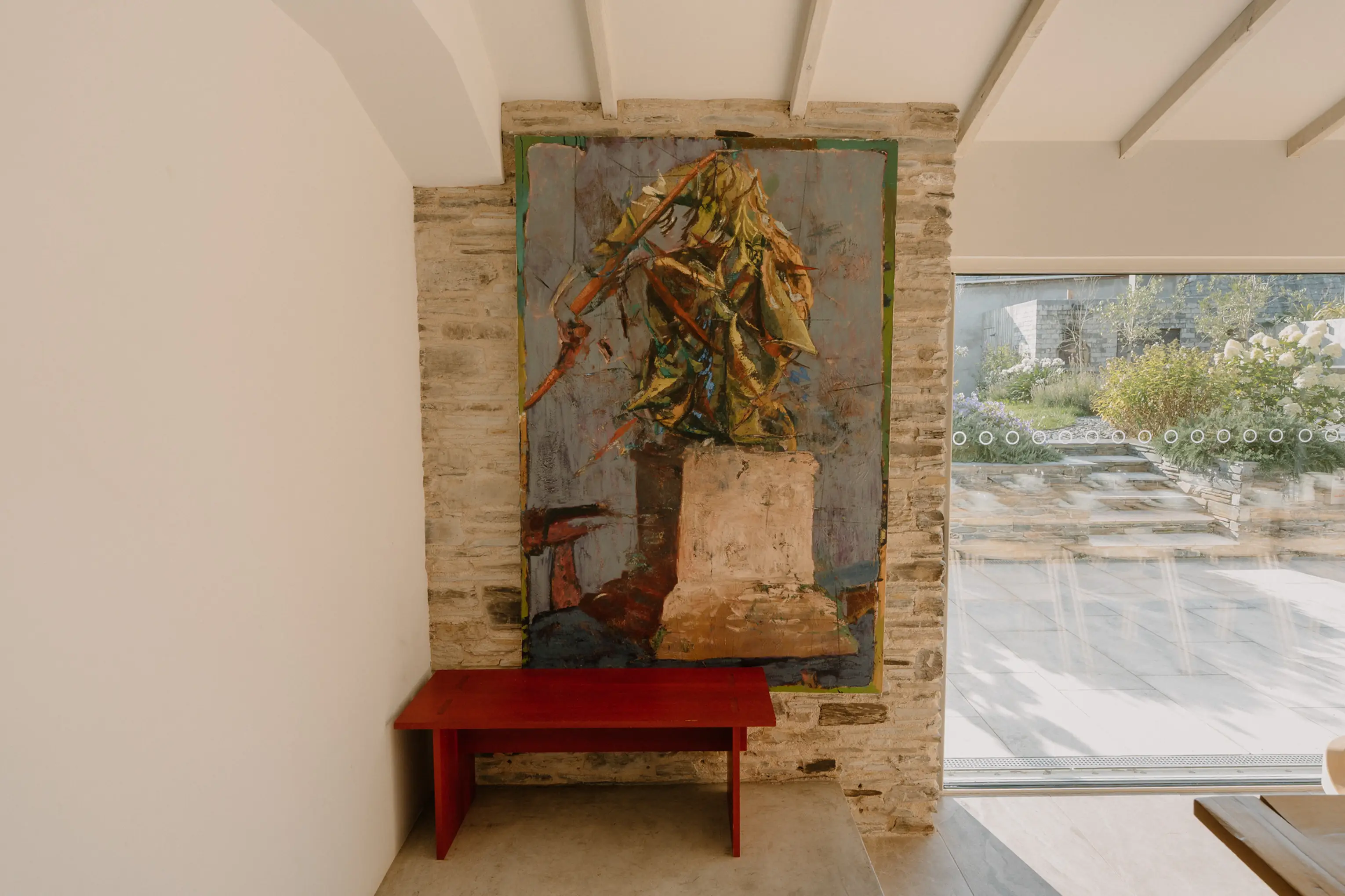 Boot room detail at ARC Padstow with a red bench, framed art and a stone wall by the garden door