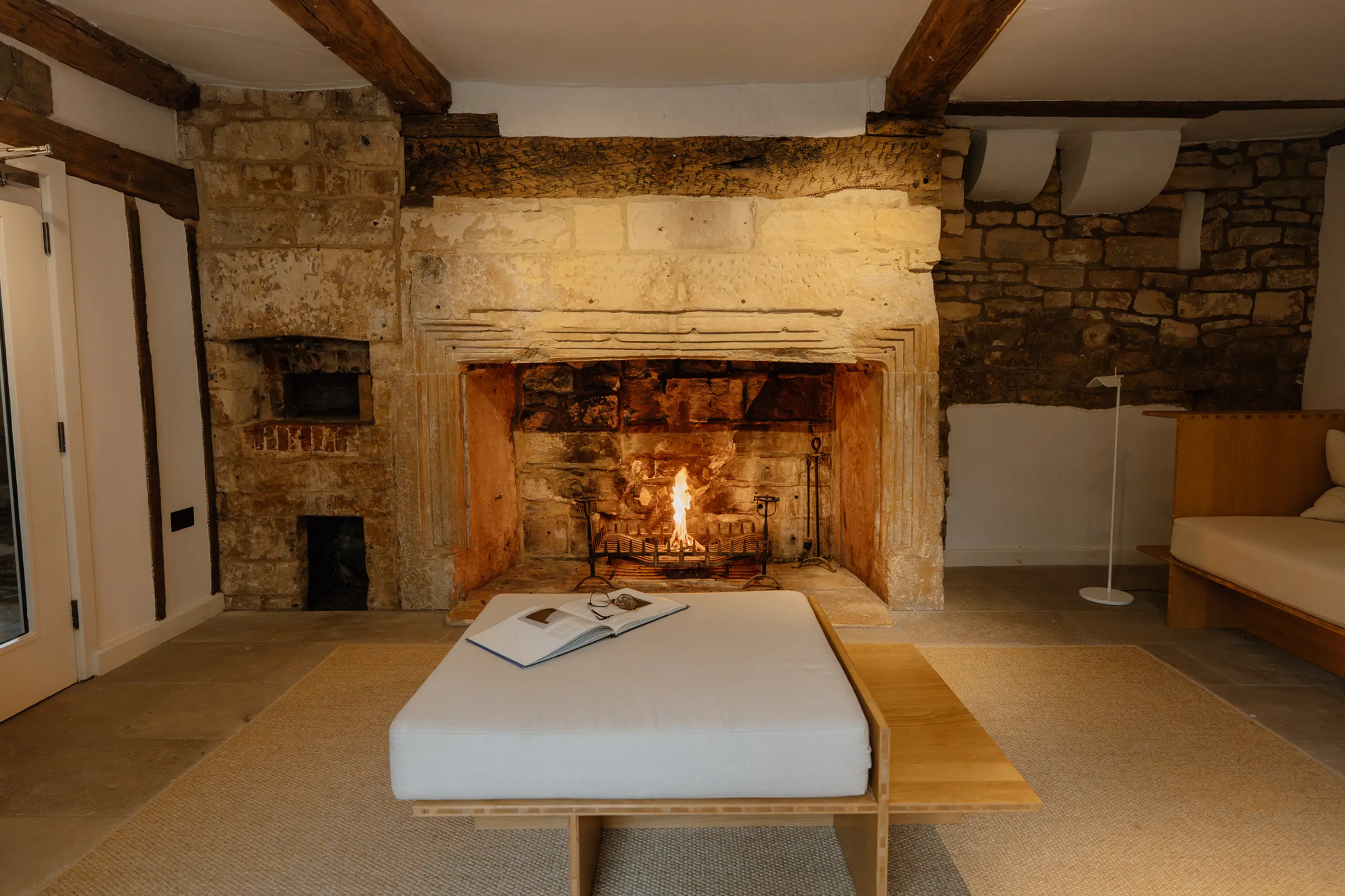 Stone fireplace with a lit fire and a bench seat in a lounge at ARC Painswick