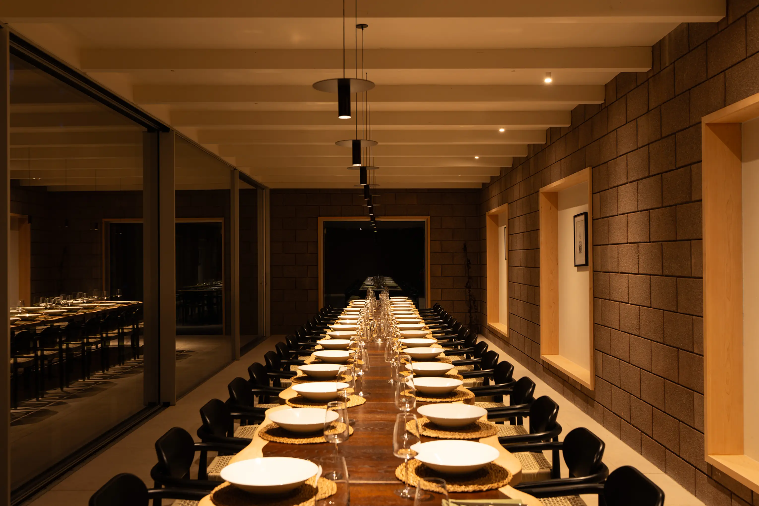 The long dining hall at ARC Peaks lit at night, laid for thirty guests with candles