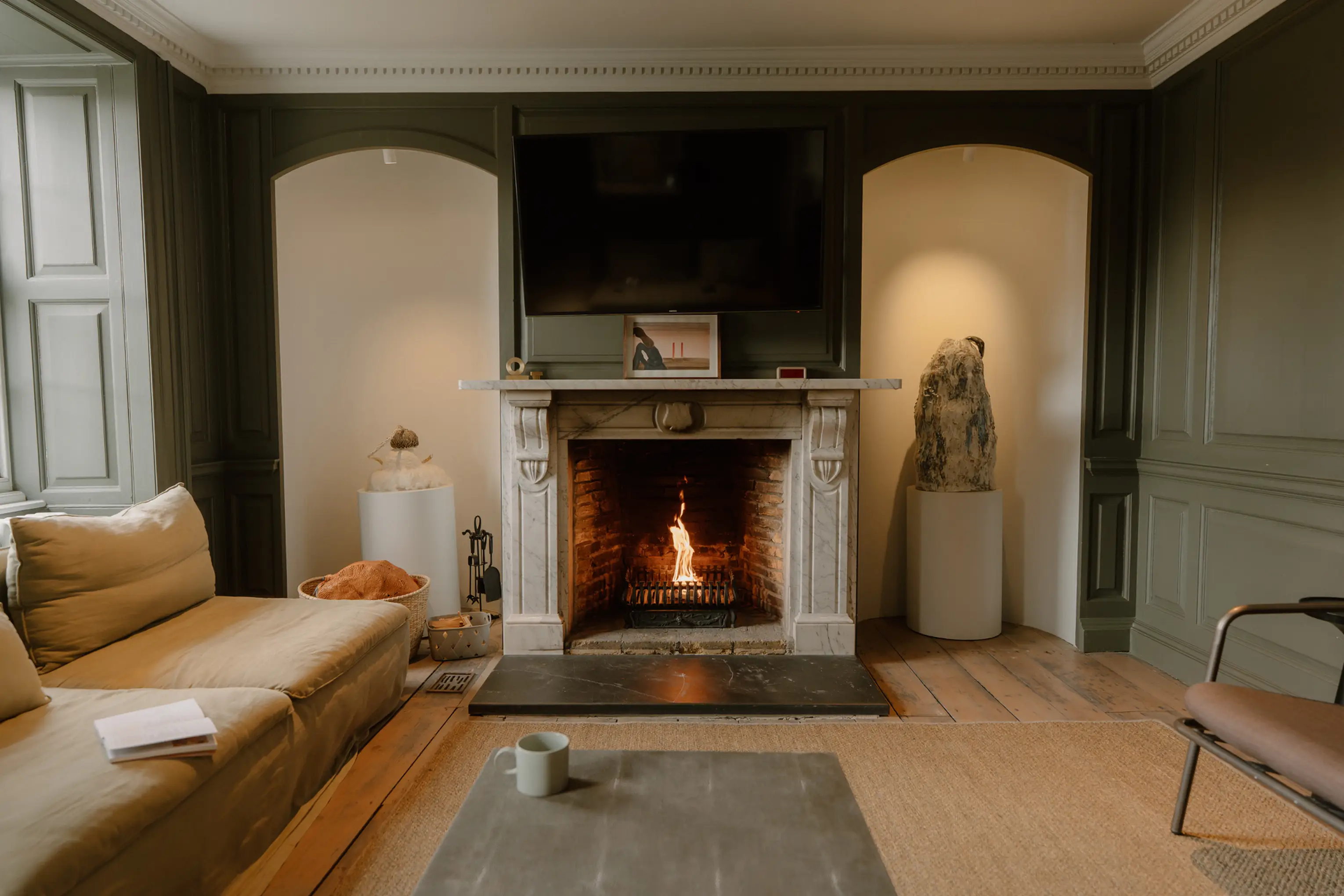 Cosy lounge at ARC Padstow with sofas around a lit open fire and arched recesses with sculptural art