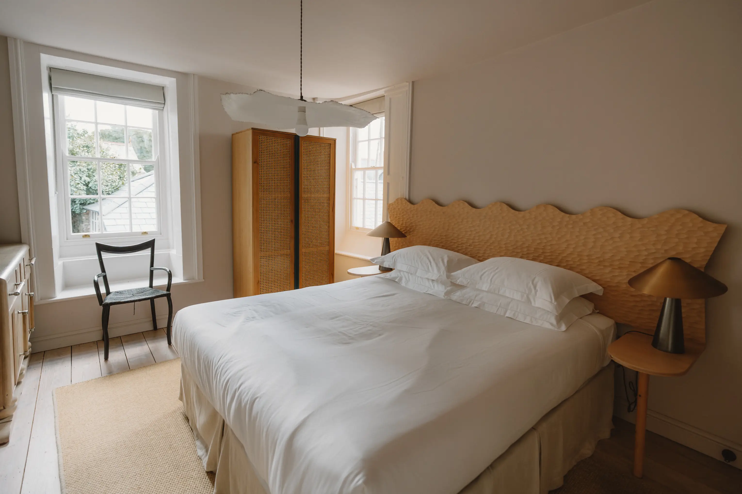 Superking bedroom at ARC Padstow with a curved timber headboard and a reading chair by the window