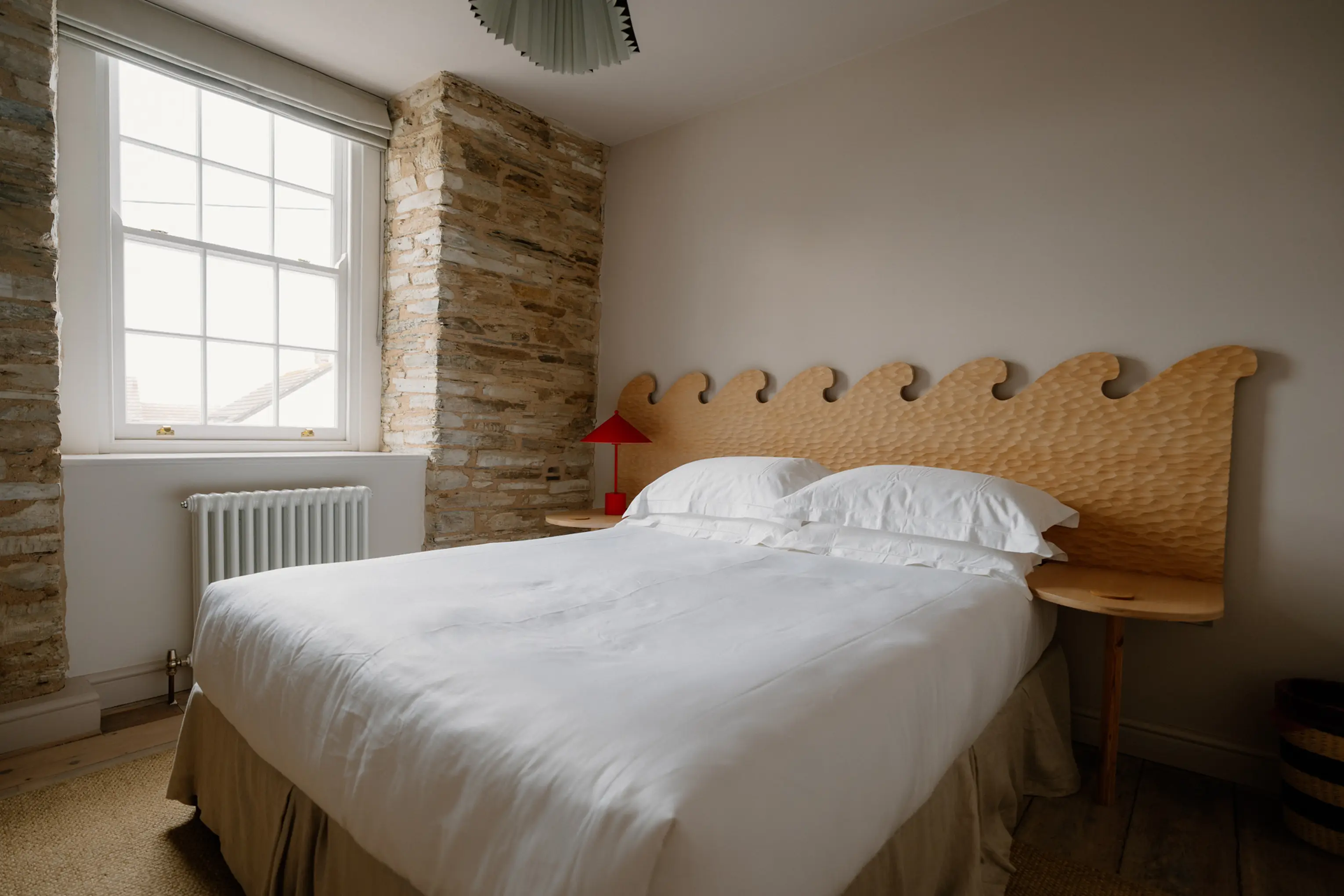 Superking bedroom at ARC Padstow with a scalloped timber headboard against an exposed stone wall