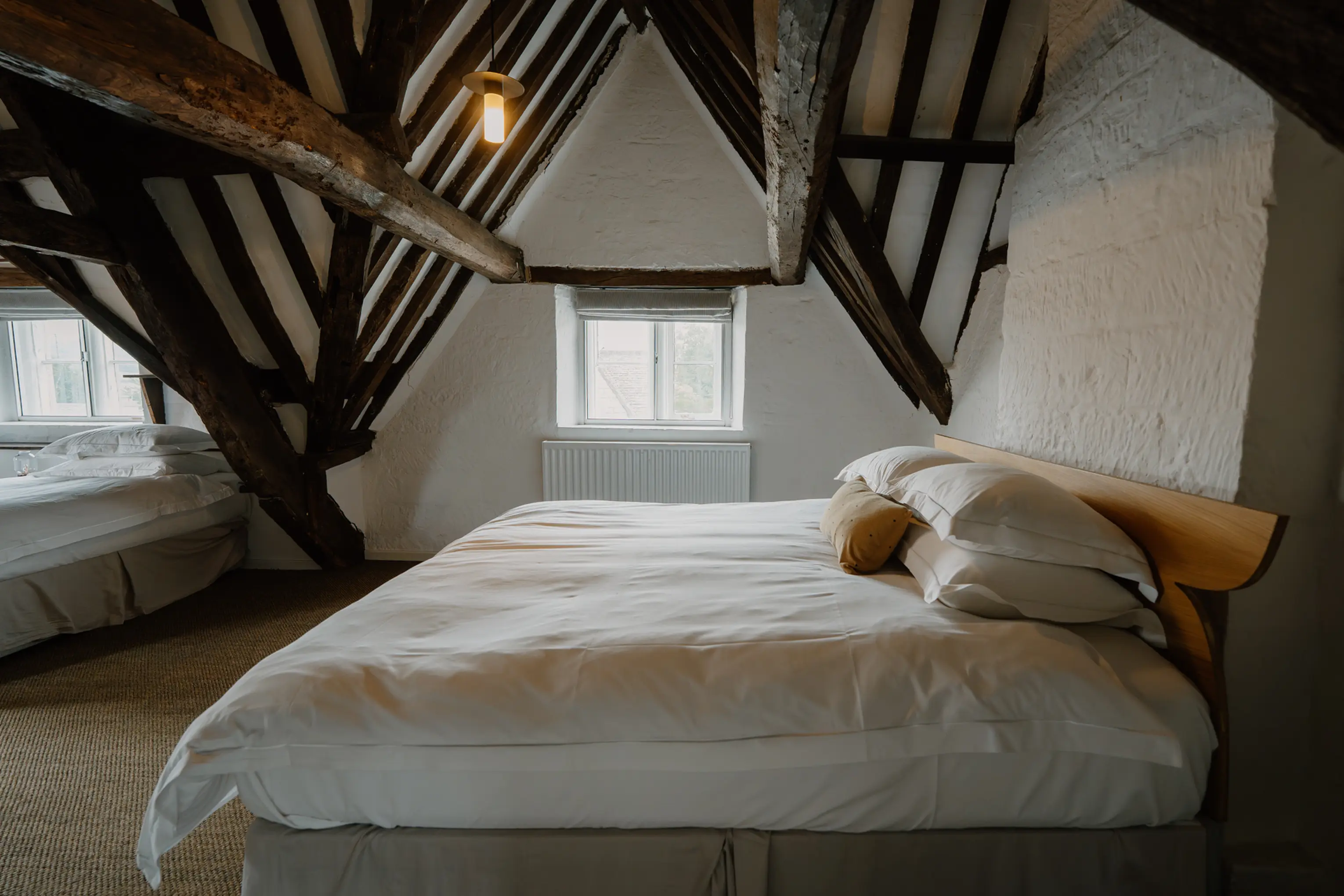 Attic bedroom at ARC Painswick with a double bed under exposed A-frame beams