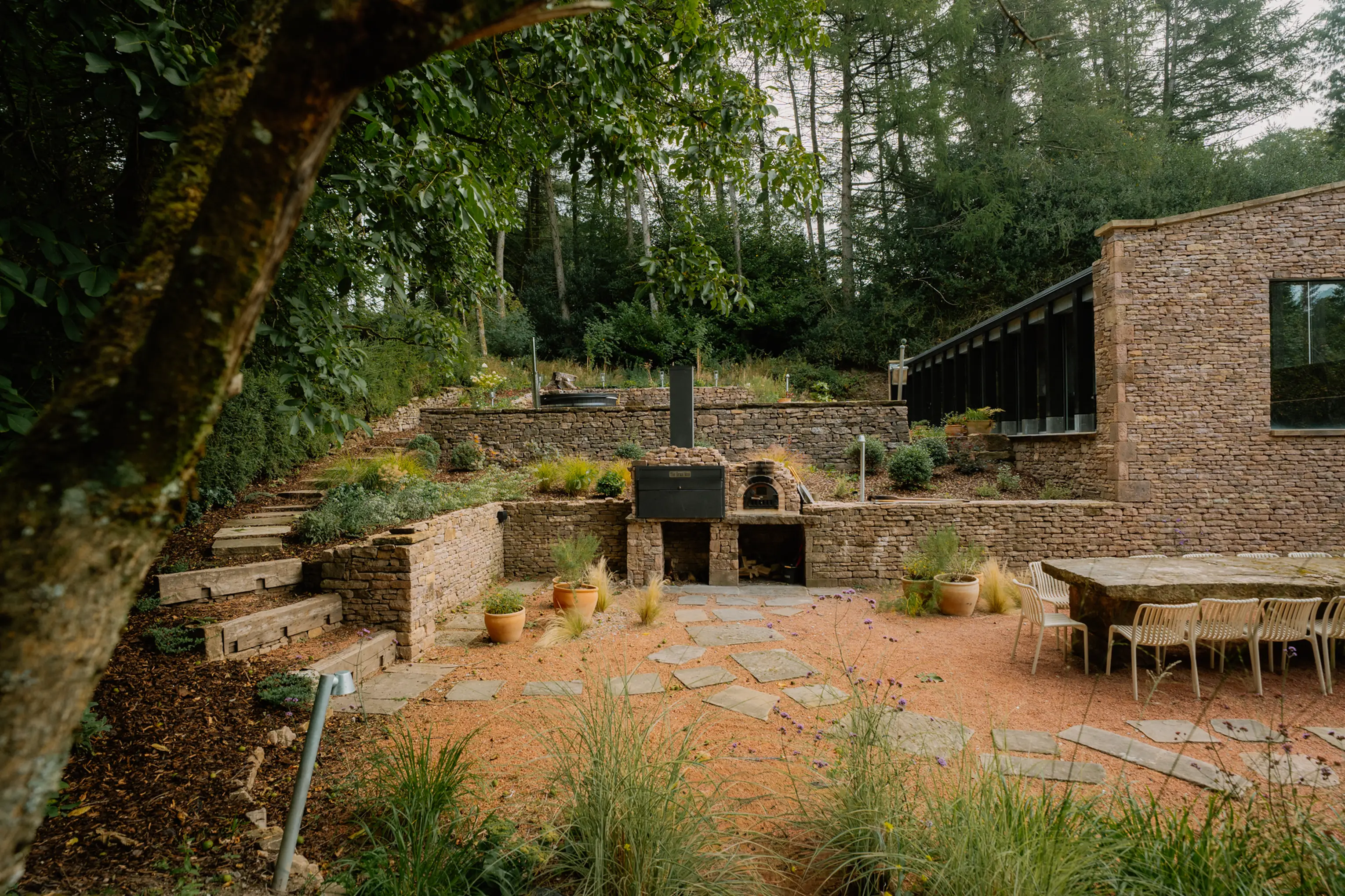 Outdoor terrace at ARC Peaks with stone seating, outdoor kitchen and planting beside the woods