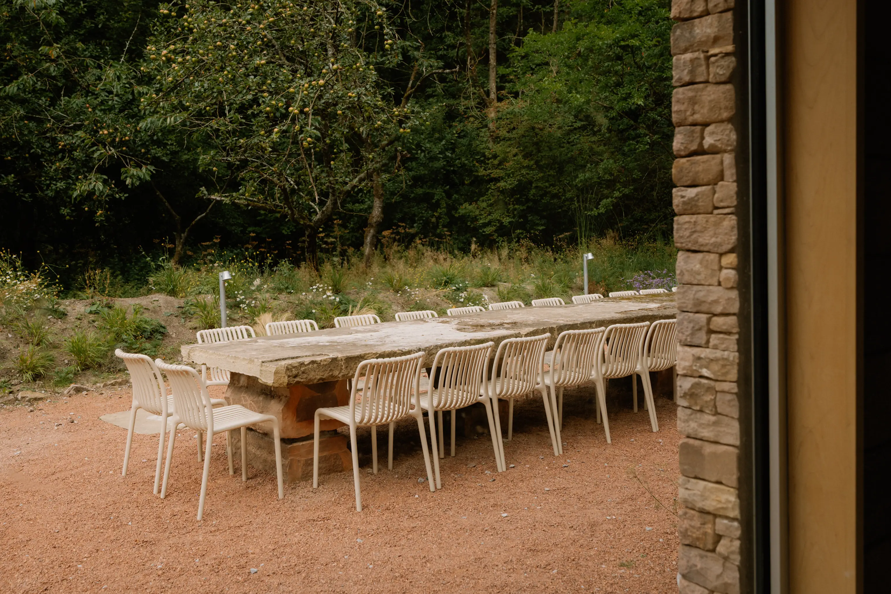 Long outdoor dining table with white chairs in the woodland garden at ARC Peaks