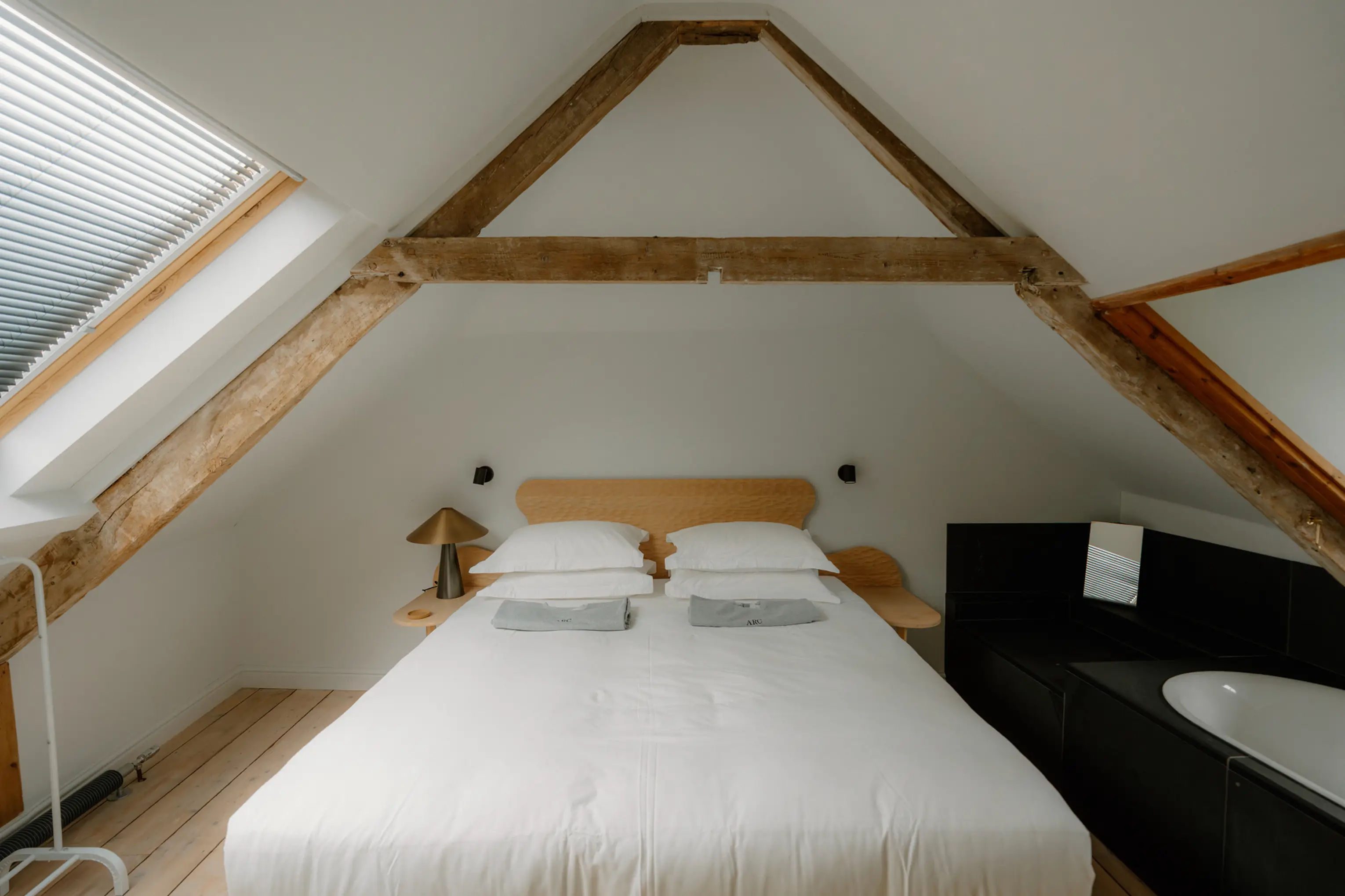 Attic bedroom at ARC Padstow with a skylight, exposed beams and a large bath