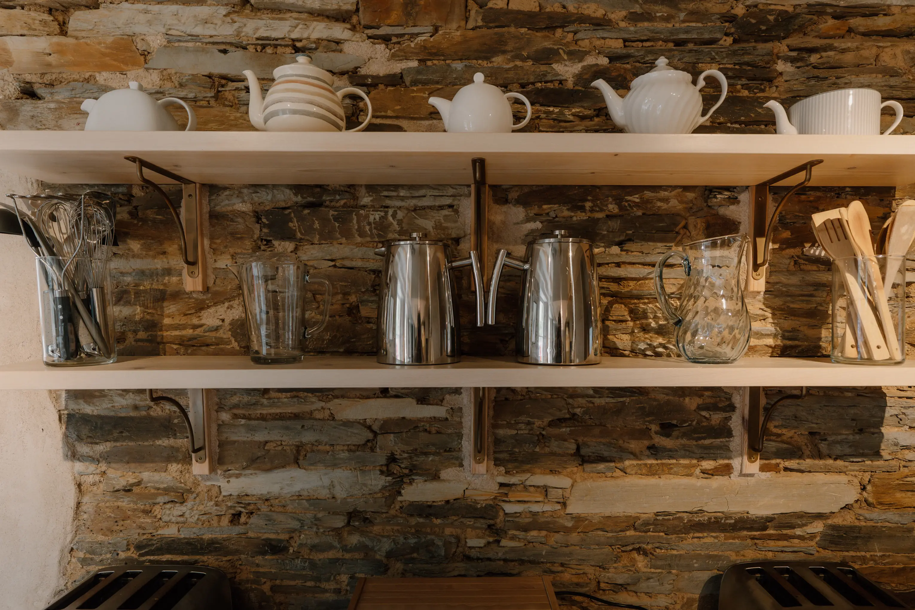 Stone-walled pantry at ARC Padstow with open shelves of crockery and a lit fire beyond