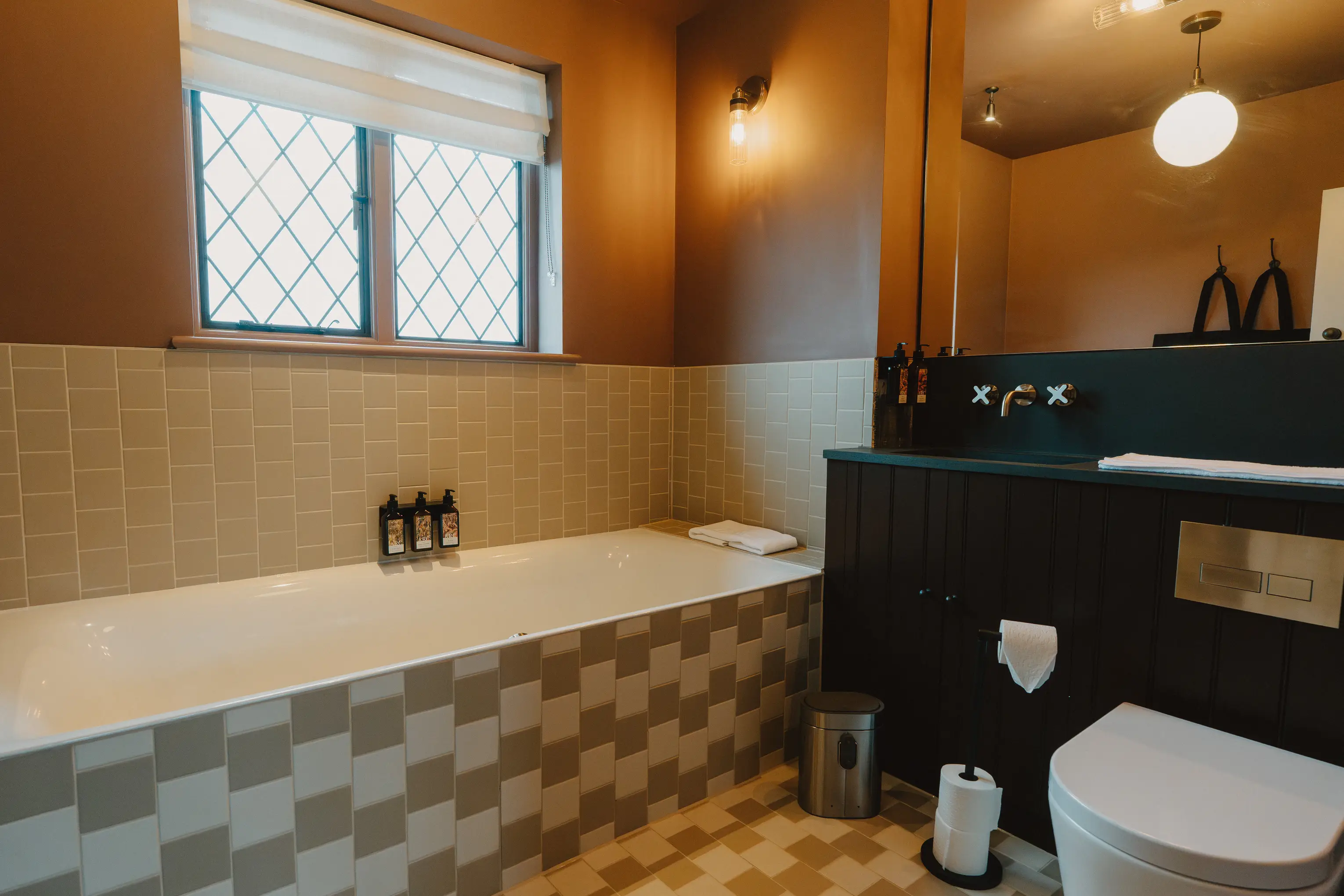 Bathroom at ARC Thorpeness with a bath, dark vanity and tiled walls