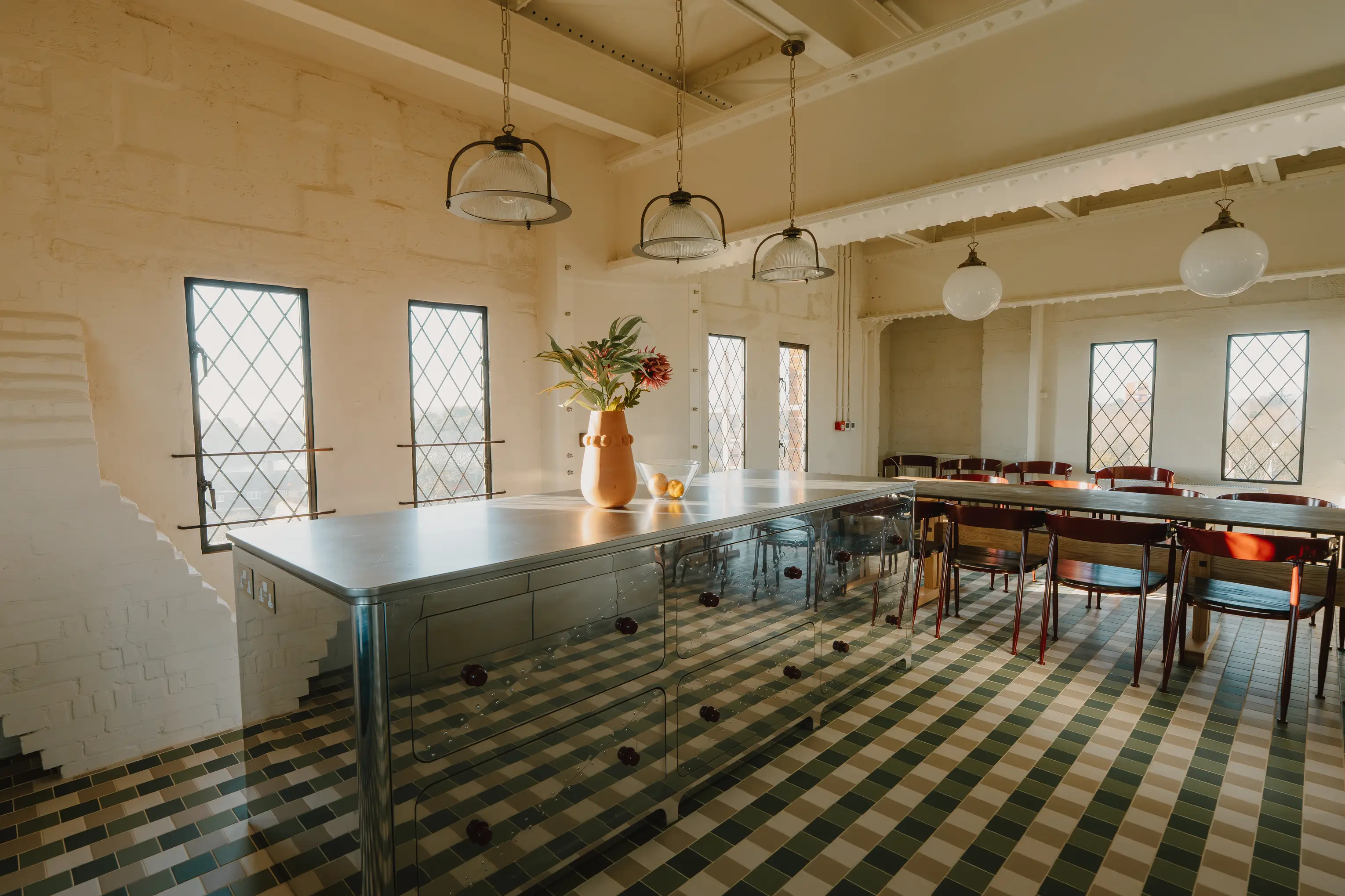 Dining area at ARC Thorpeness with a long table, steel kitchen counter and a patterned tiled floor