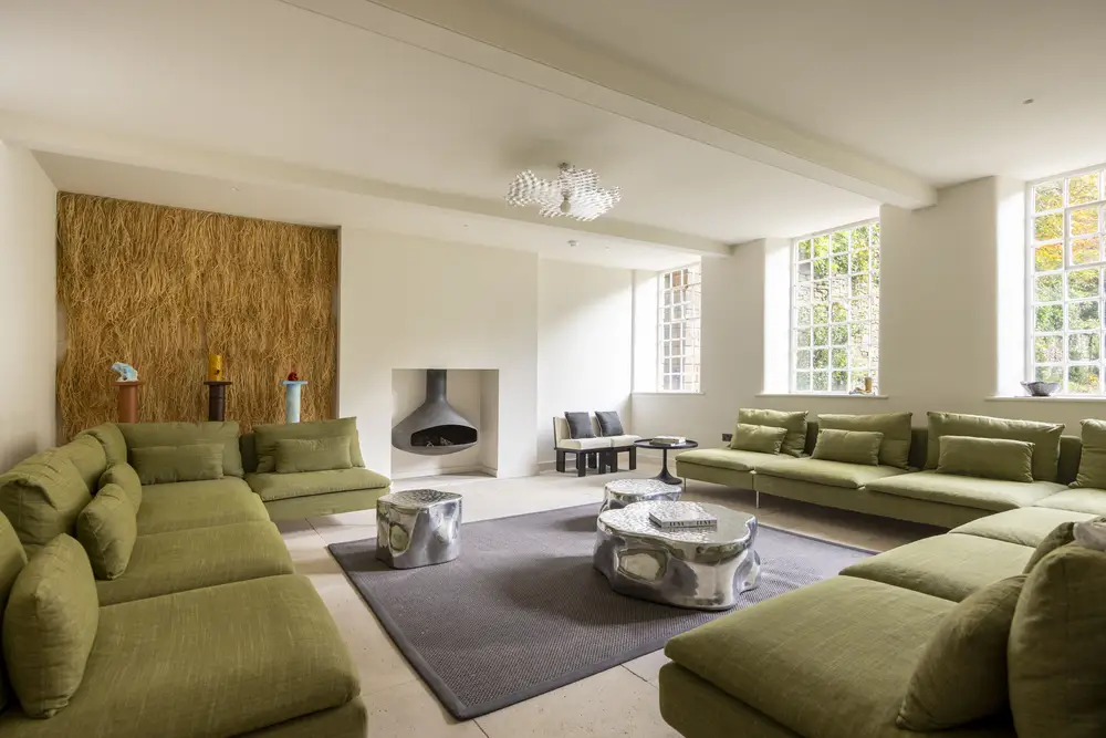A spacious living room designed custom for group stays in the Peak District, with a modern fireplace, abstract coffee table, large windows, and a textured accent wall.