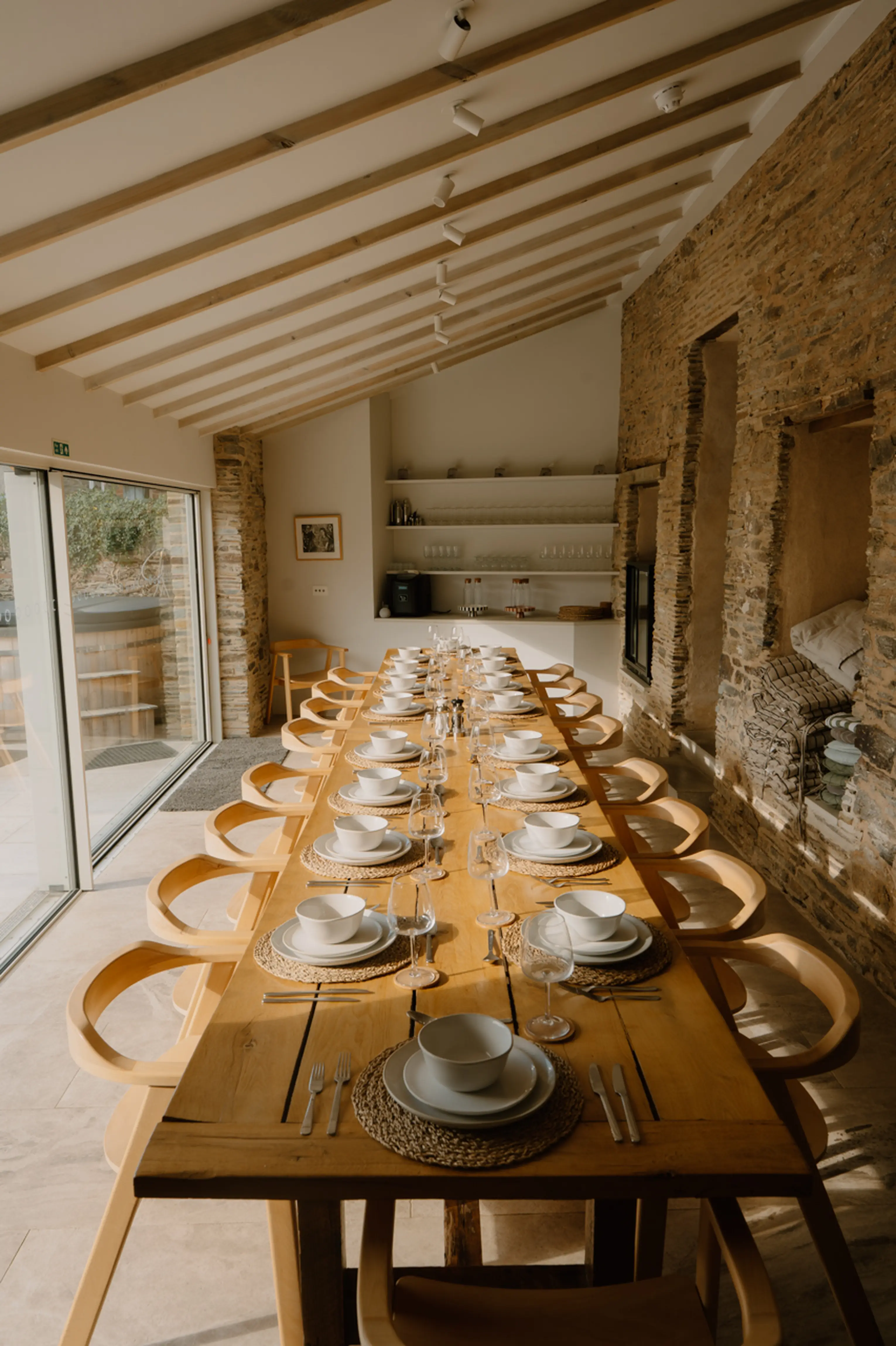 Long indoor dining table laid for a group at ARC Padstow, with glass doors opening to the garden