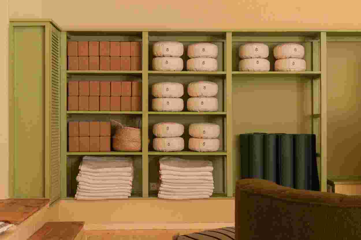 Shelves with neatly stacked yoga mats, towels, bolsters, and boxes in a calming, organized space with green accents.
