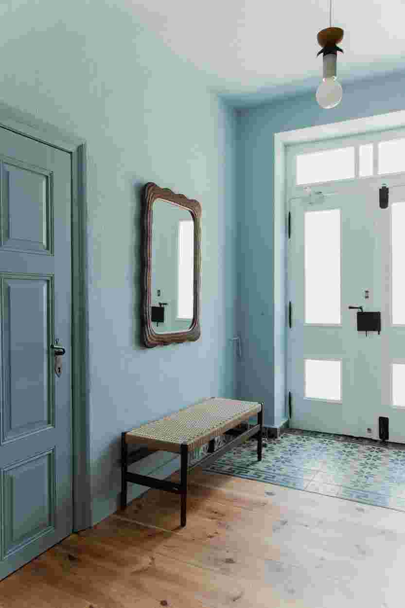 A light blue hallway with a wooden floor, a bench, a decorative mirror, and a white door with frosted glass panels.