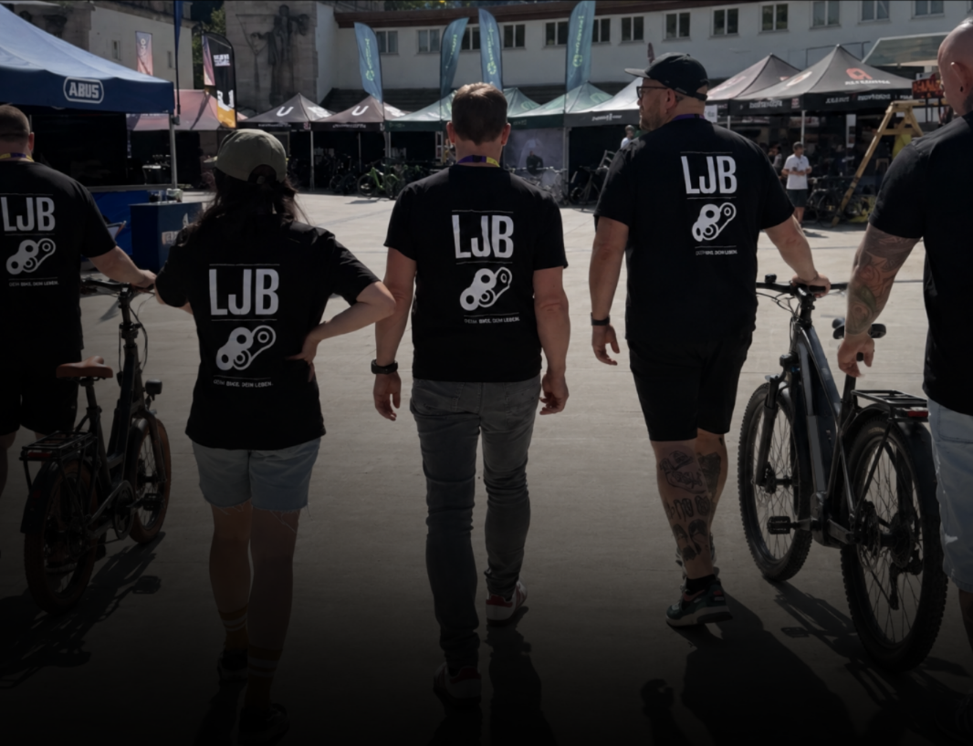 Gruppe in schwarzen LJB-Shirts läuft mit Fahrrädern zwischen Messeständen auf einem Festgelände