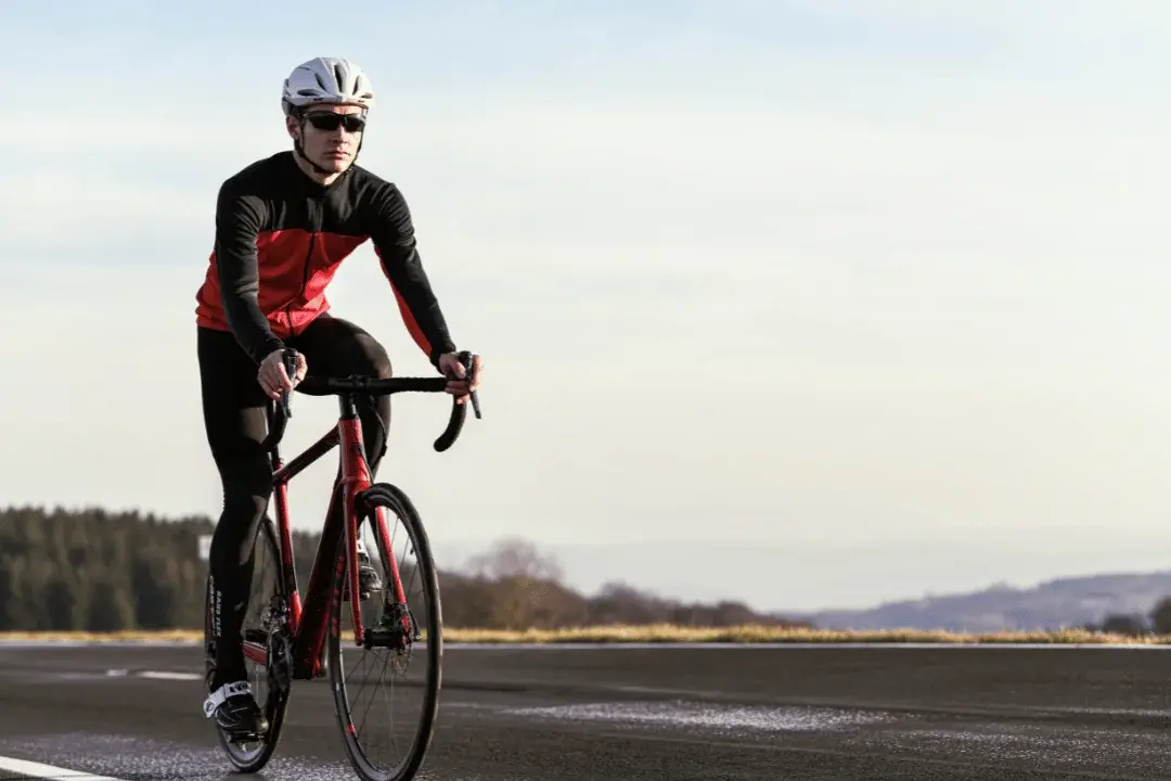 Ein Radfahrer in rot-schwarzem Sportoutfit und Helm fährt auf einem asphaltierten Radweg in winterlicher Landschaft.