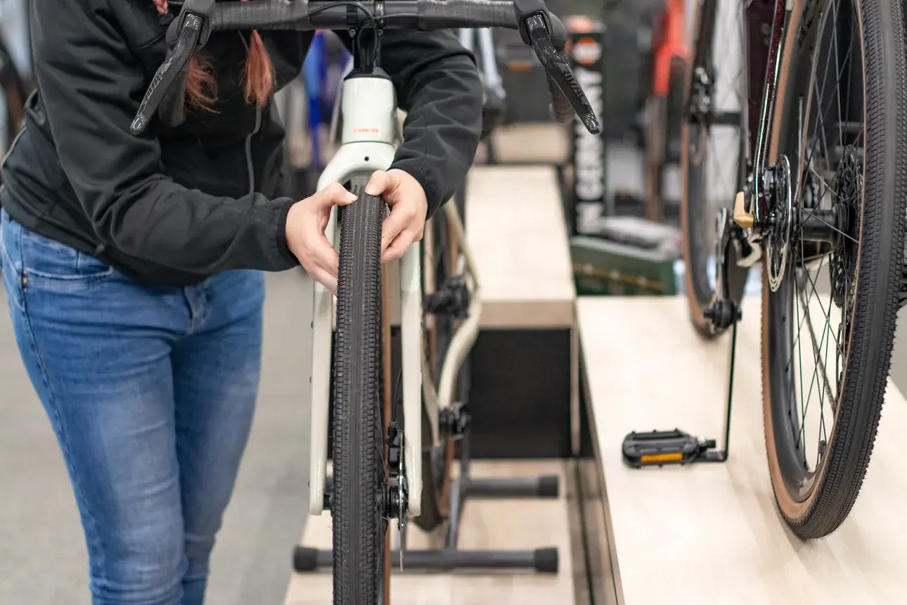 Eine Frau begutachtet die Reifenbreite eines Gravelbikes im Fahrradladen.