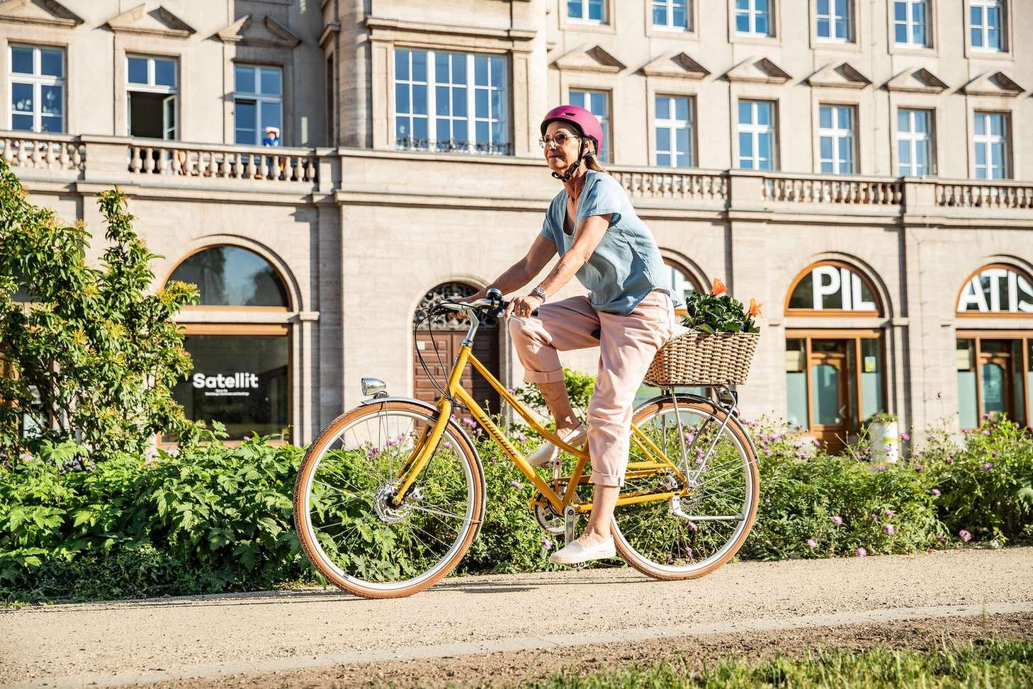 Frau mit einem Citybike und einem Korb voller Einkäufe.