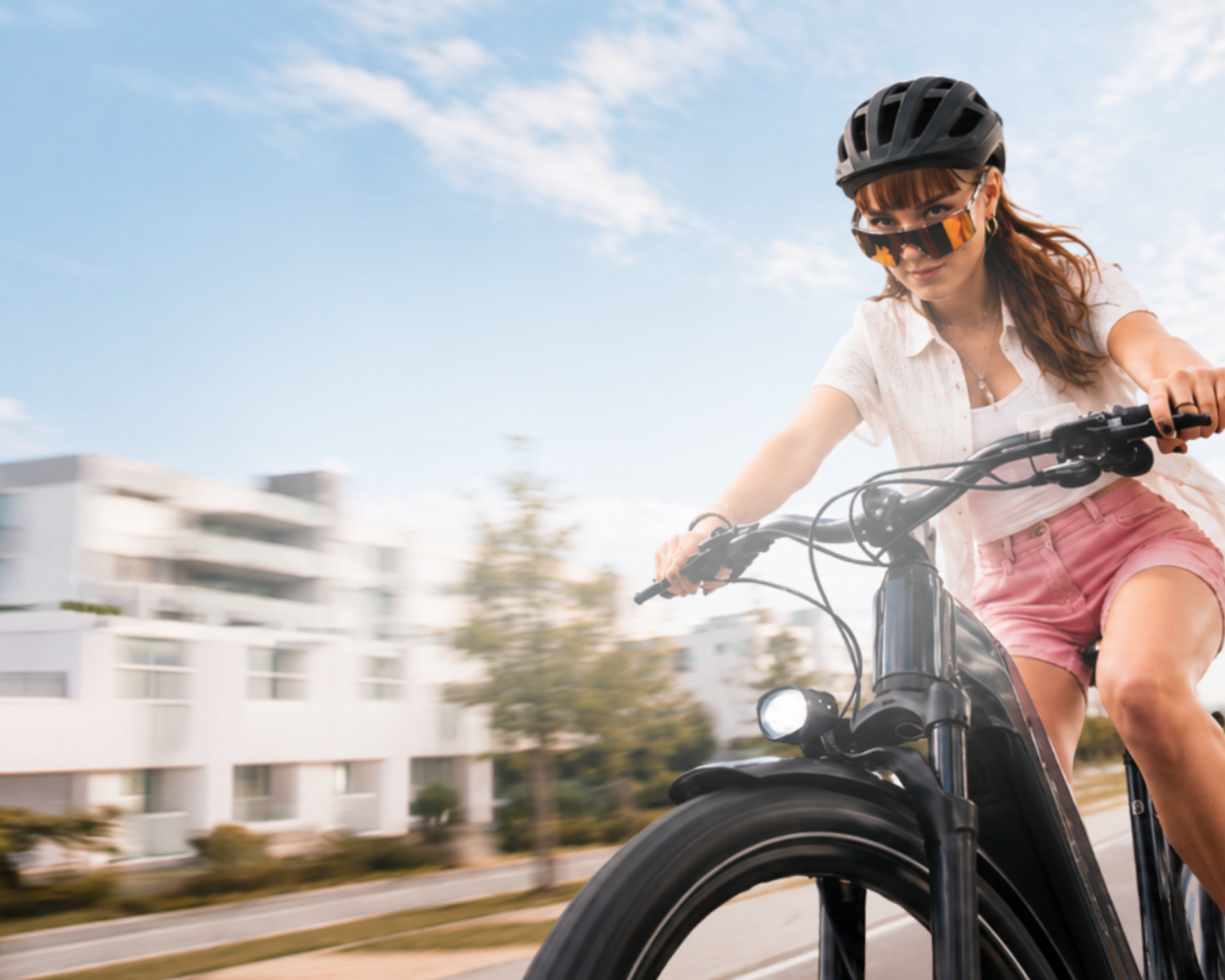 Frau mit Helm und Sportbrille fährt ein schwarzes E-Bike auf einer Straße