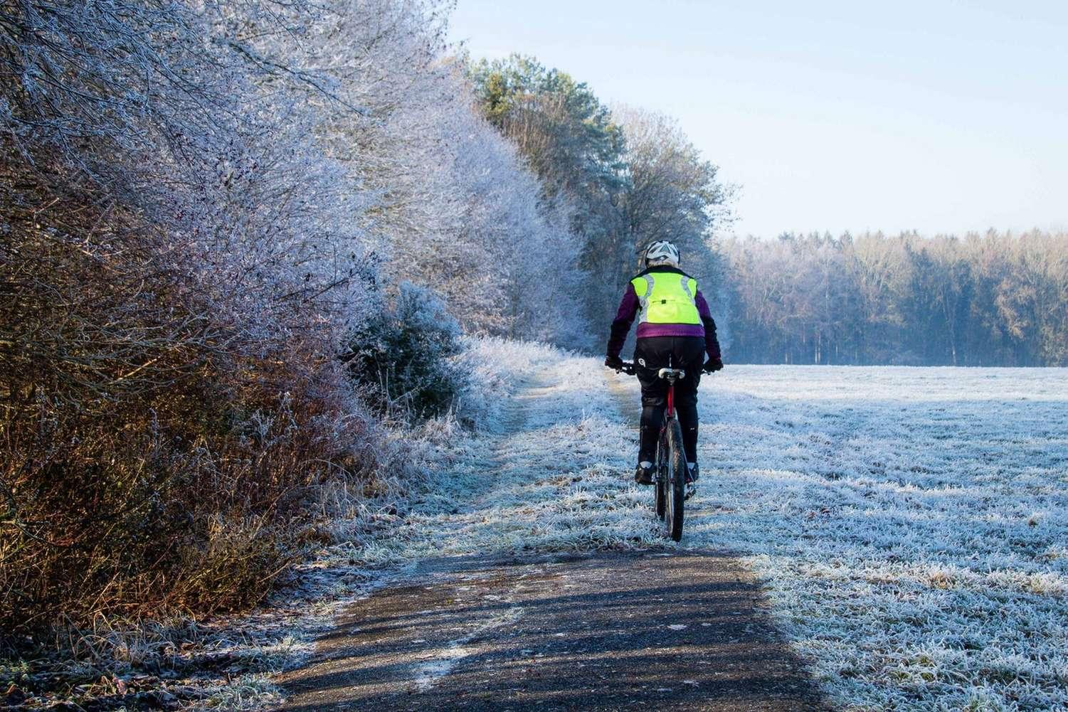 Frostige Landschaft mit einem Radfahrer mit Warnweste im Winter