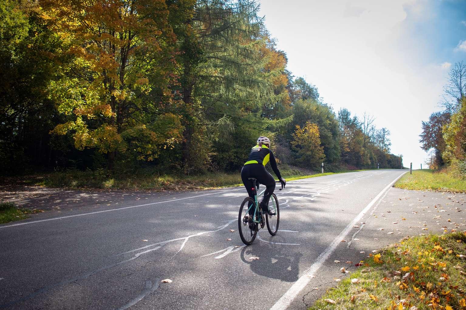 Radfahrerin im Herbst auf dem Rennrad mit einer gelb-schwarzen sichtbaren Jacke.