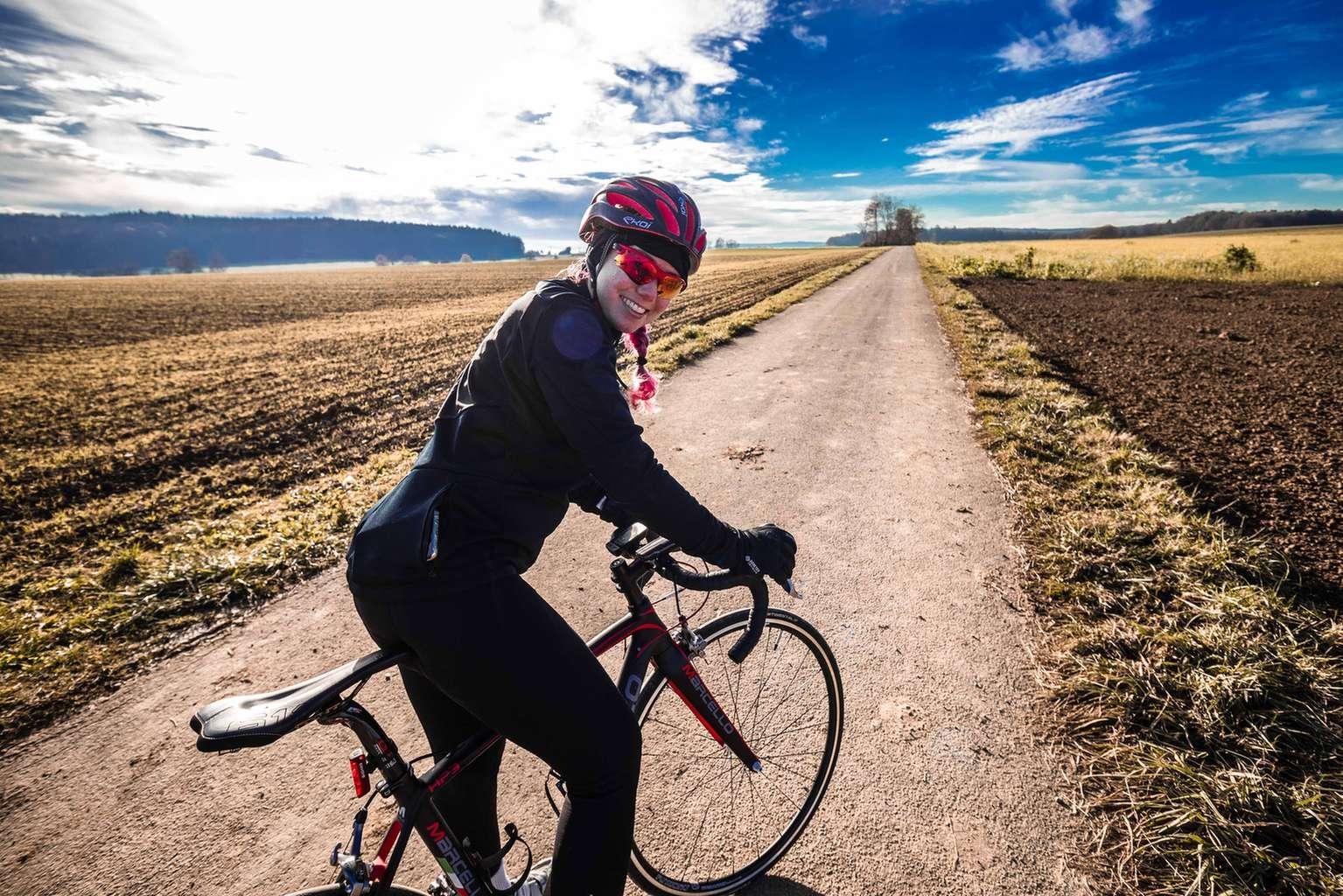 Rennradfahrerin lächelt in die Kamera unter strahlend blauem Himmel