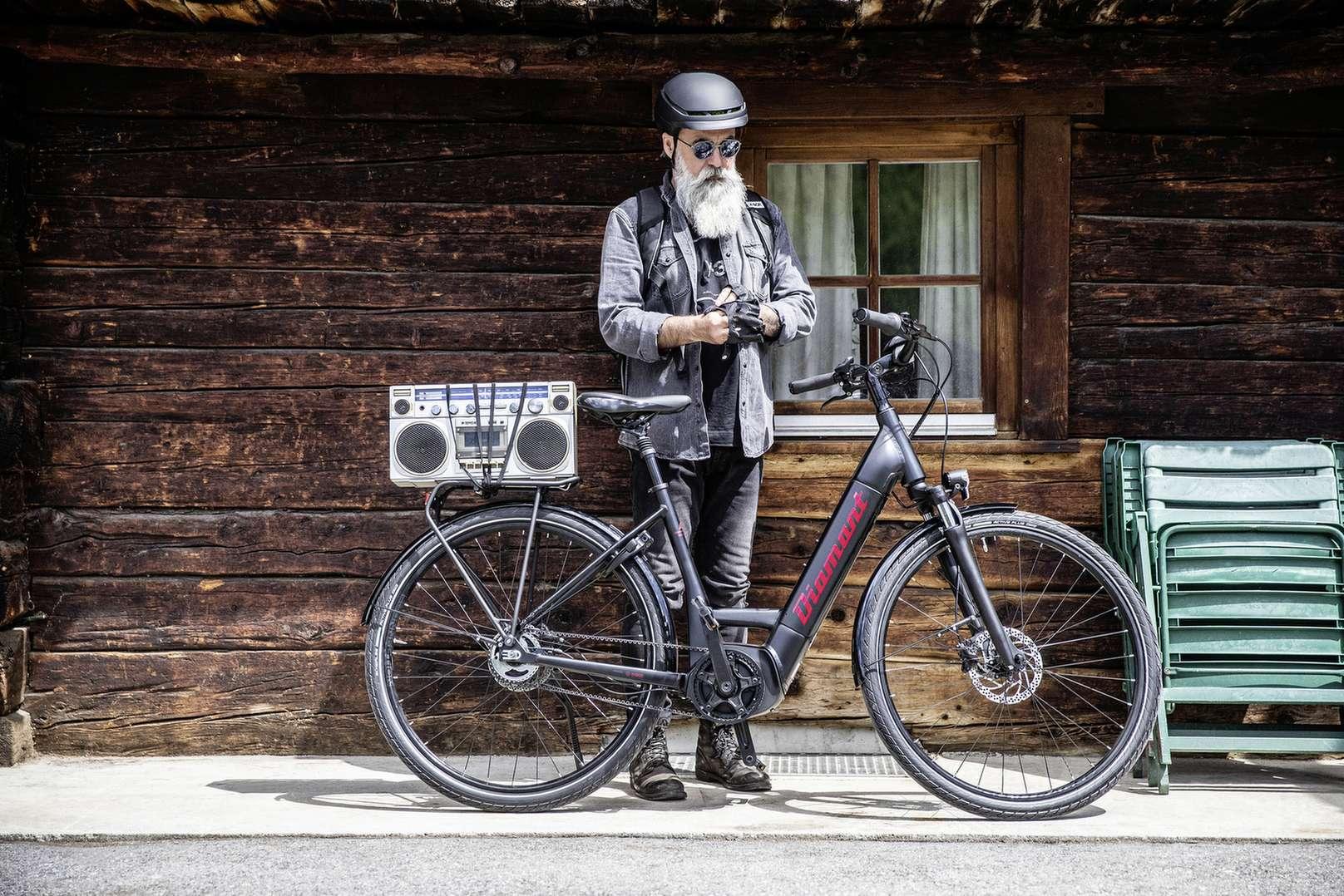 E-Biker steht neben dem Fahrrad und hat eine Musikbox auf dem Gepäckträger.