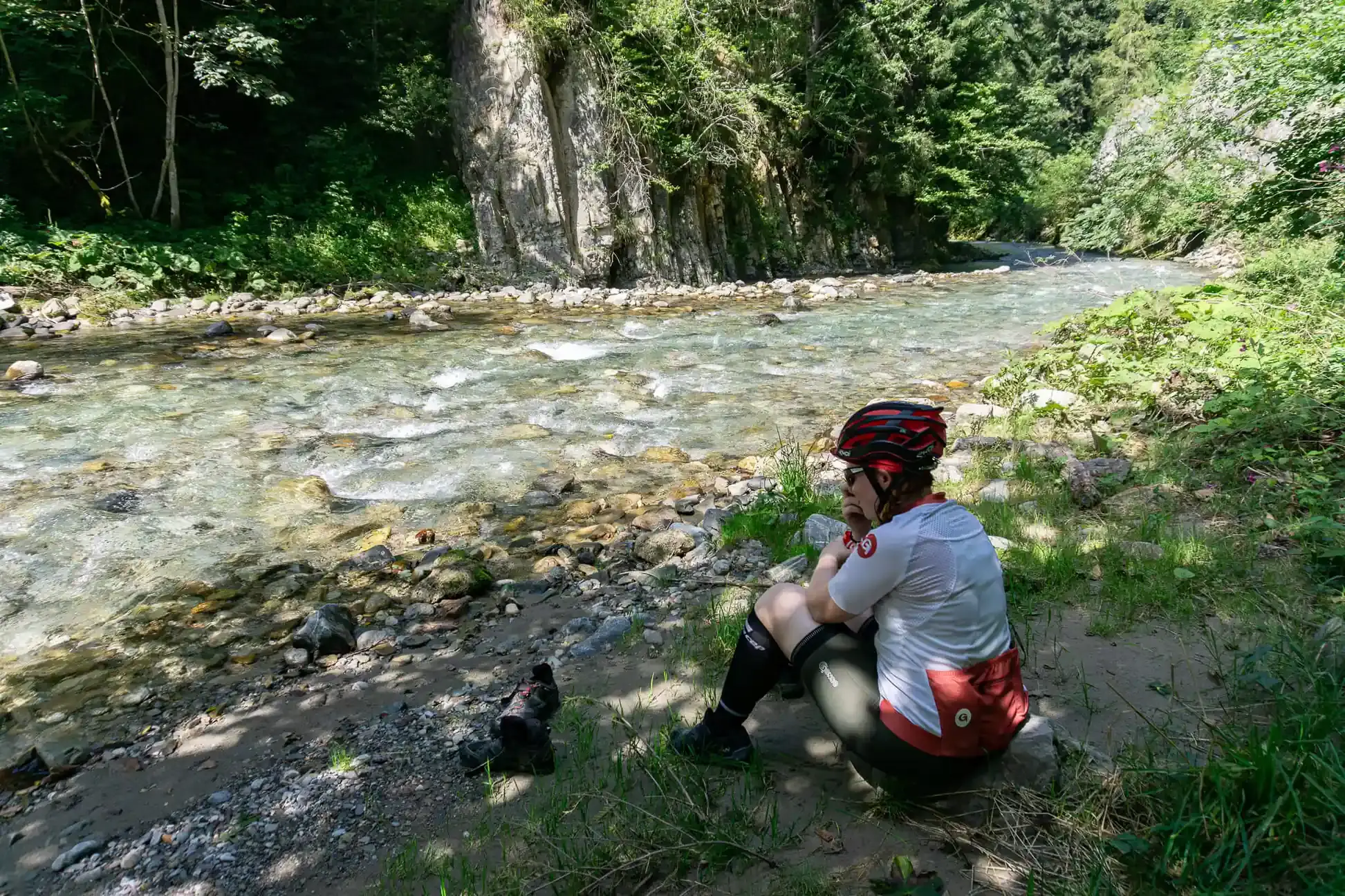 Radfahrerin macht eine Pause an einem Fluss und isst einen Apfel.