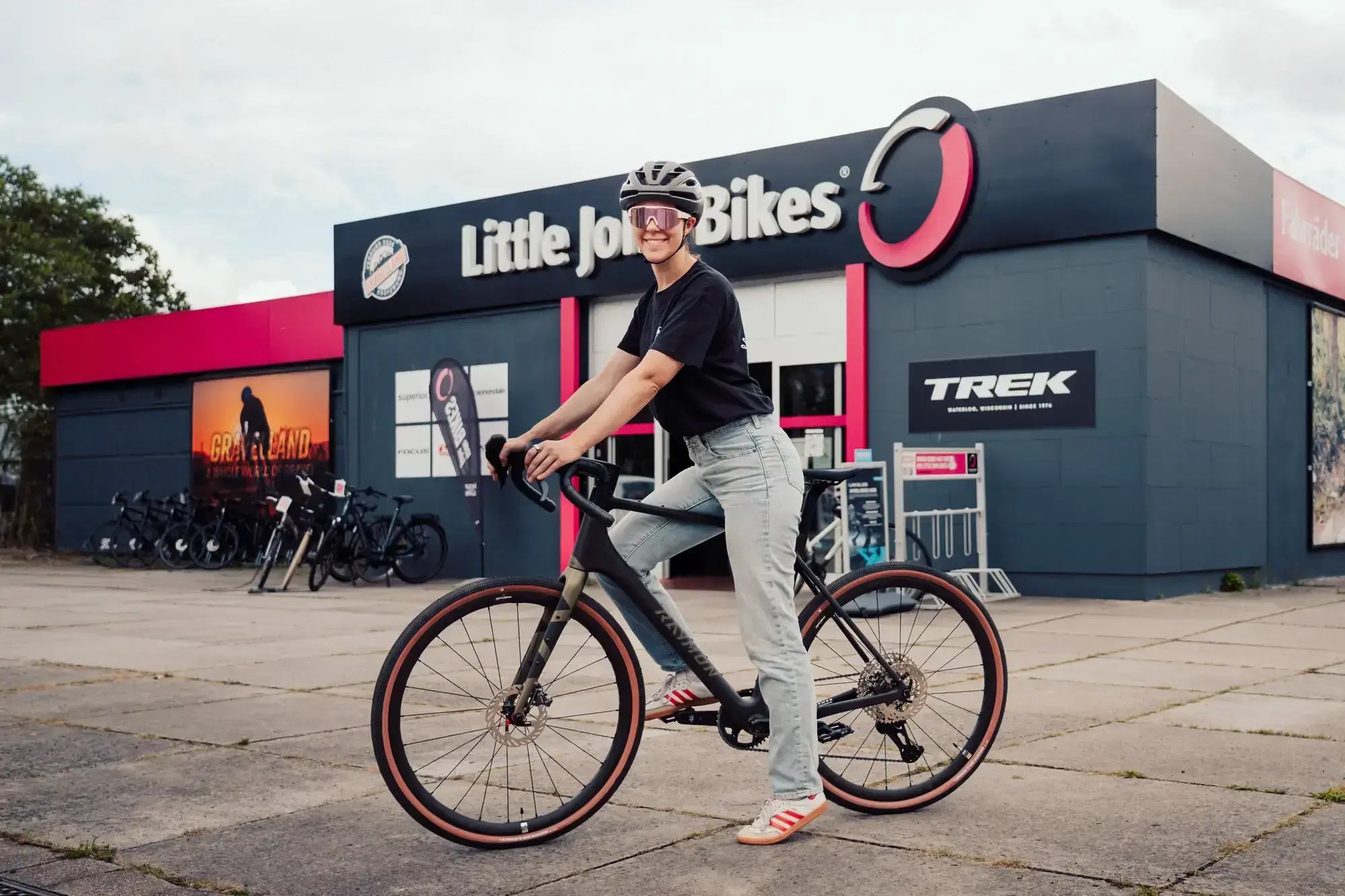 Radfahrerin steht mit einem Gravelbike zur Probefahrt vor einer Filiale von Little John Bikes