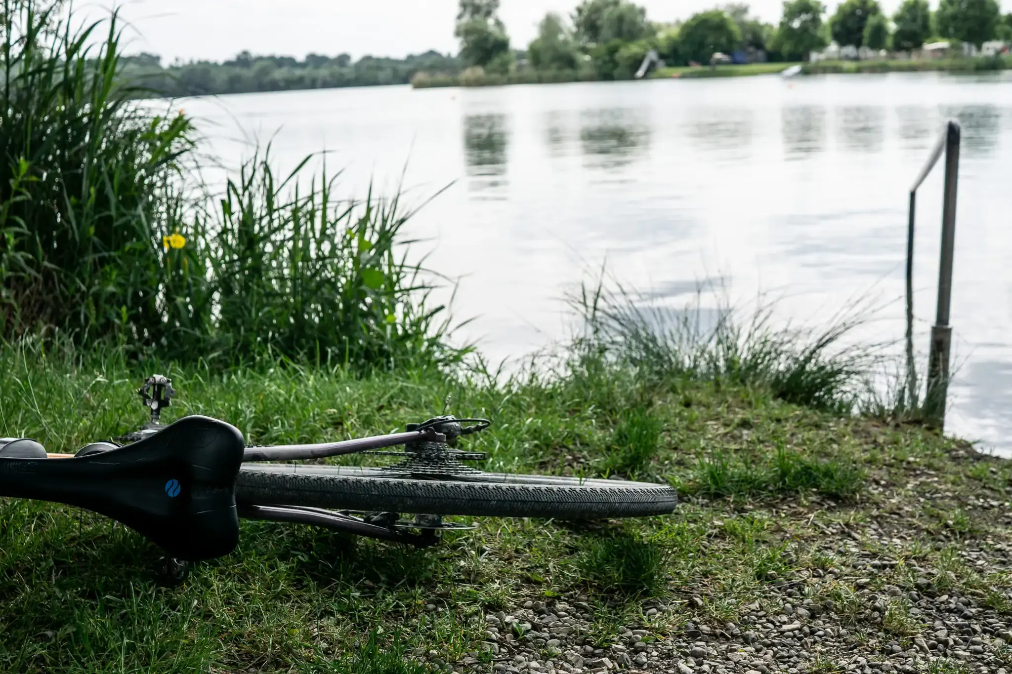 Ein Fahrrad liegt auf einer Wiese im Vordergrund, im Hintergrund ein Badesee.