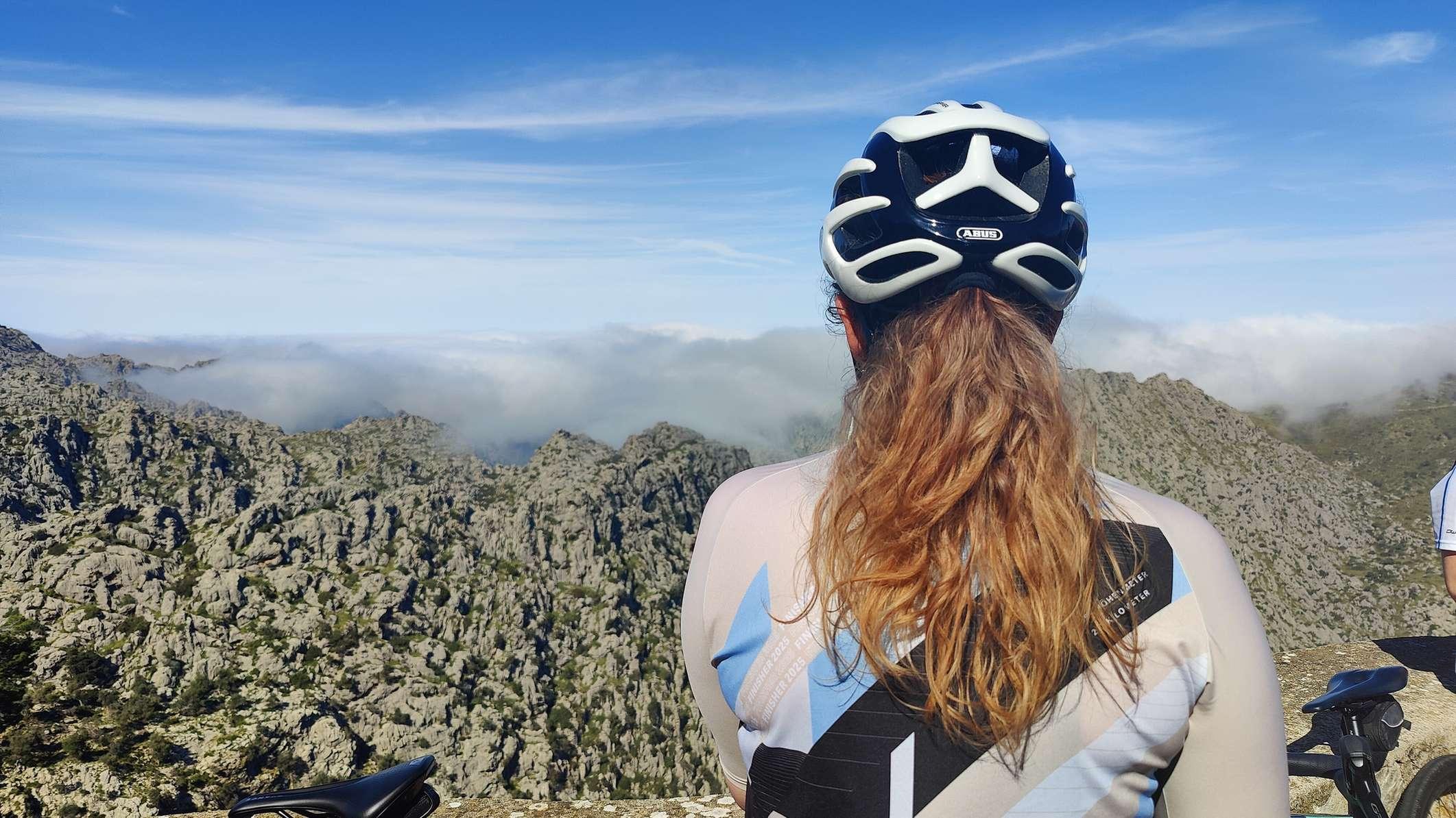 Frau mit Fahrradhelm blickt in eine Berglandschaft.