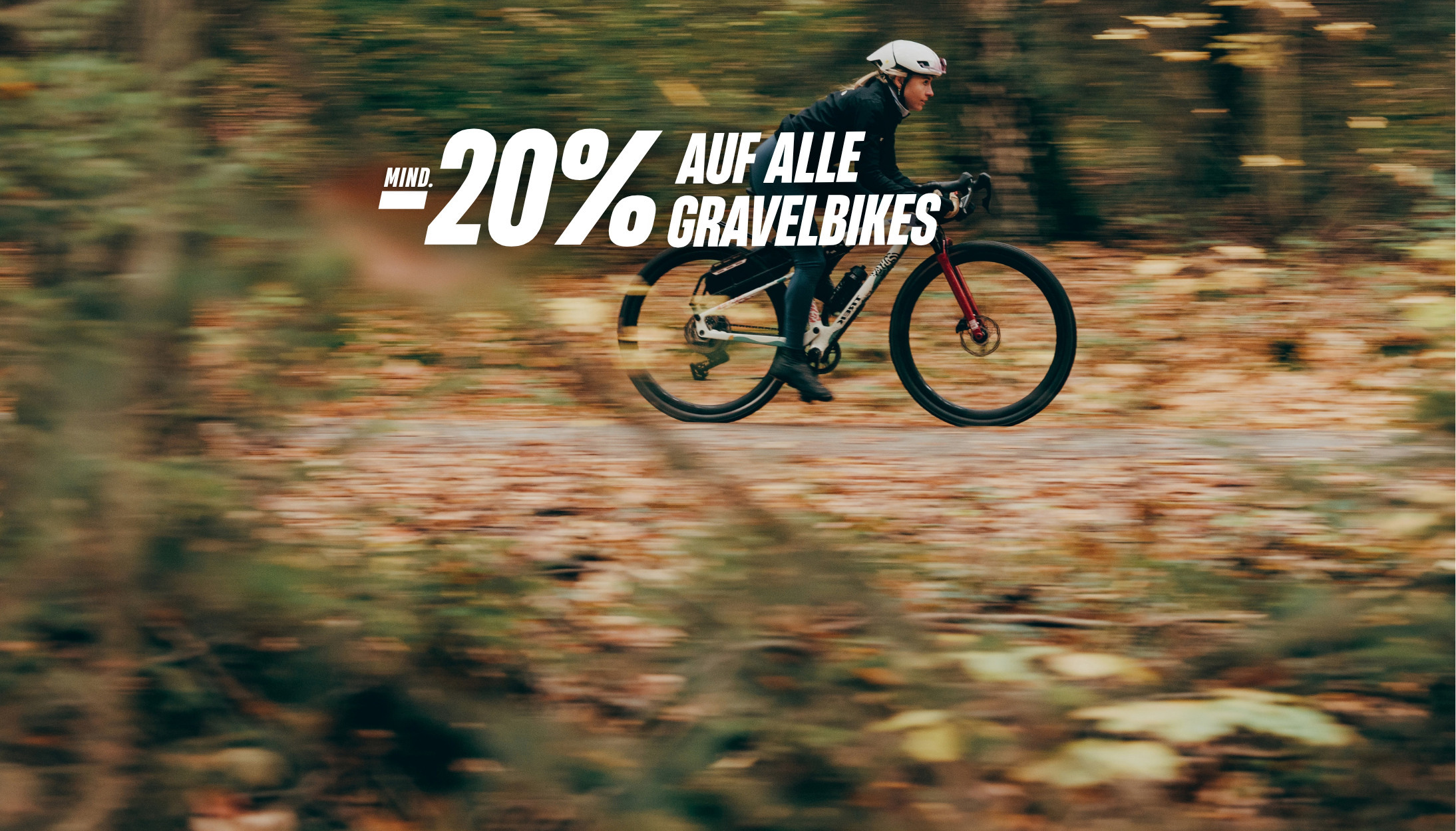 Frau auf einem Gravelbike fährt über einen Waldweg. Rabattaktion: „Mindestens 20 % auf alle Gravelbikes“