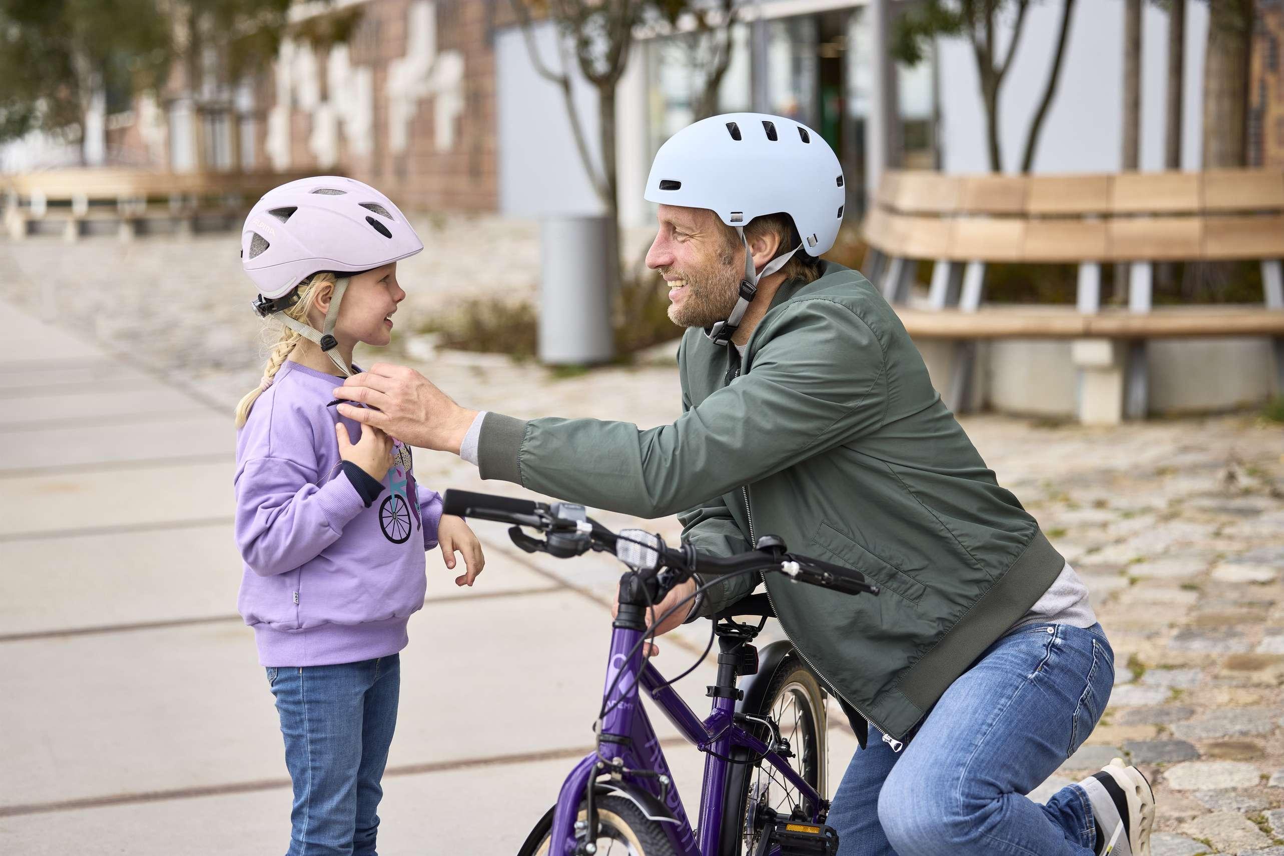 Ein Vater hilft seiner Tochter, ihren Fahrradhelm zu justieren.