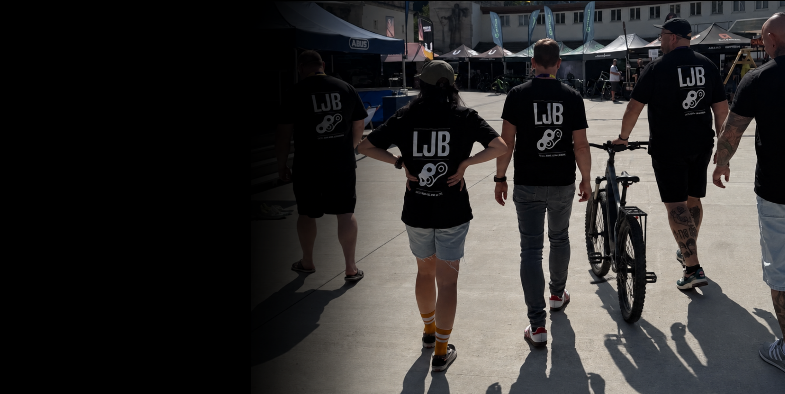 Fünf Kollegen in schwarzen LJB-Shirts gehen mit Fahrrädern über ein Festgelände.