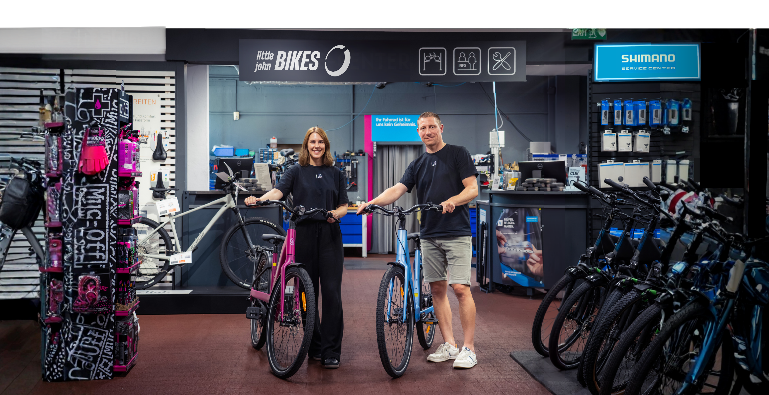 Zwei Mitarbeitende stehen mit einem pinken und einem blauen E-Bikes in der gut ausgestatteten Little John Bikes Filiale.
