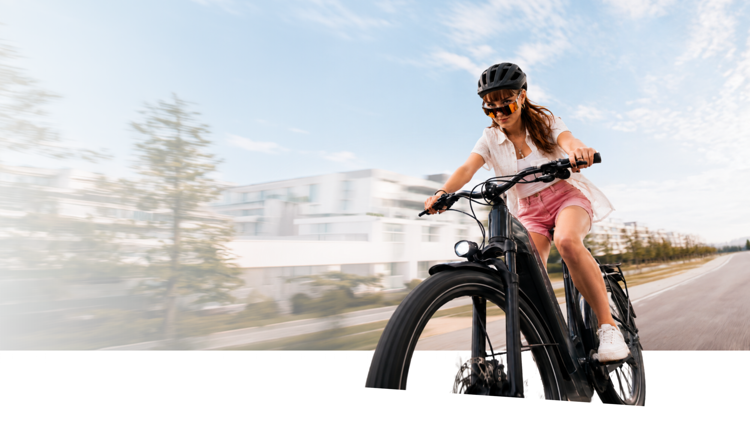 Frau mit Helm und Sportbrille fährt ein schwarzes E-Bike auf einer Straße
