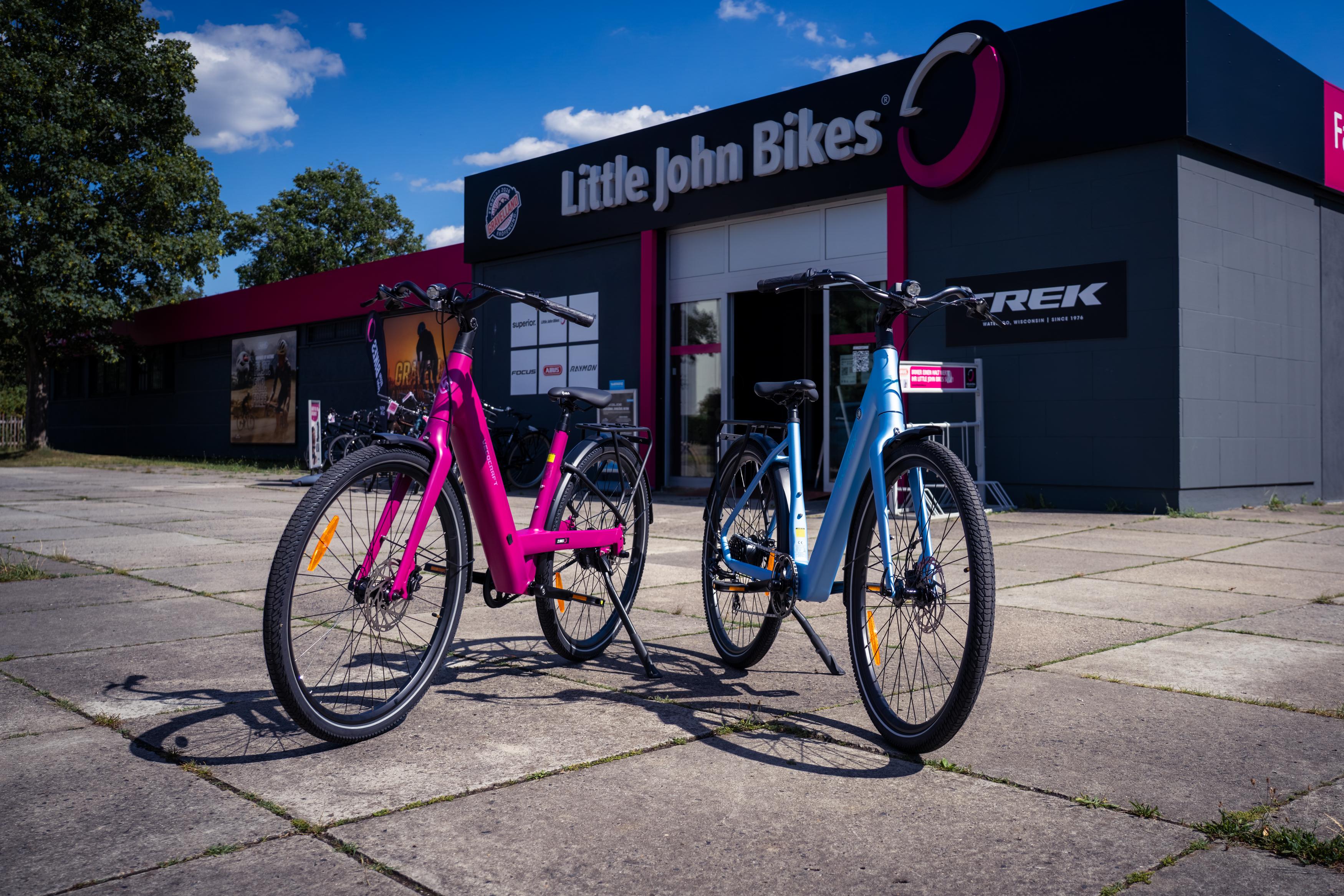 Pinkes und blaues E-Leihräder vor der Filiale Little John Bikes bei sonnigem Wetter
