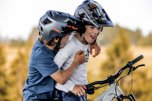 Zwei Kinder tragen Helme und fahren gemeinsam auf einem Fahrrad.