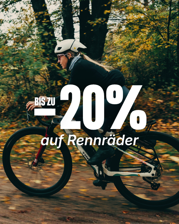 Radfahrerin mit weißem Helm fährt auf einem Rennrad durch den Herbstwald. Text: „Bis zu 20 % auf Rennräder“.