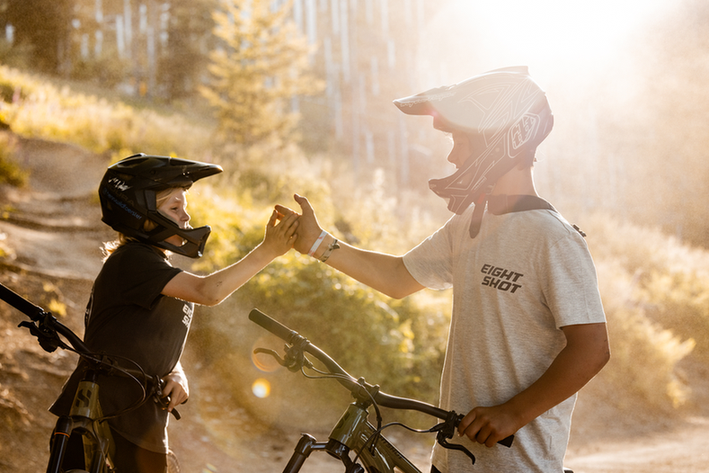 Zwei Mountainbiker geben sich einen High-Five auf einem sonnigen Waldweg.