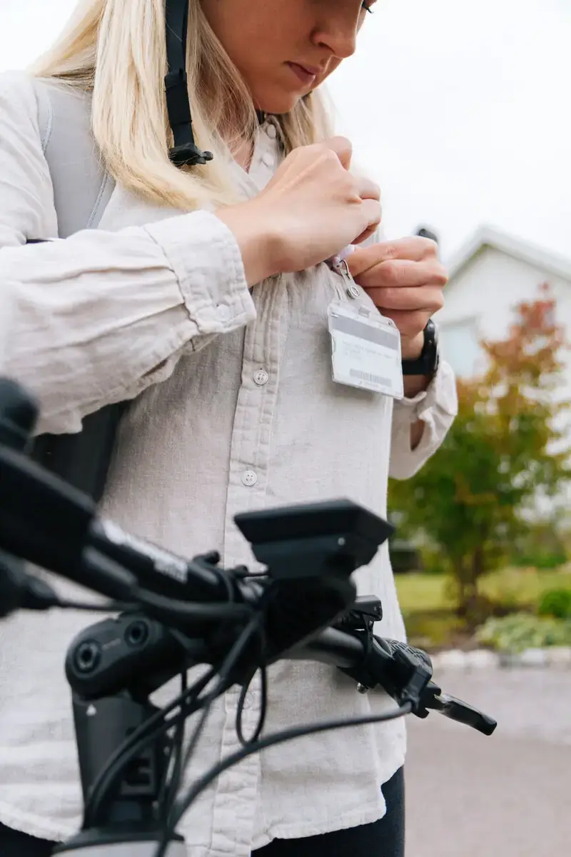 Frau klemmt sich einen Firmenausweis an ihr Hemd und steht vor einem Fahrrad.